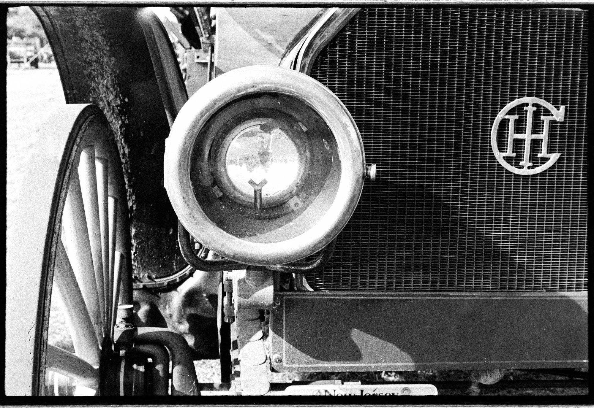 Black and white photo of the photographer reflected in the headlight of a 1900s International Harvester truck.