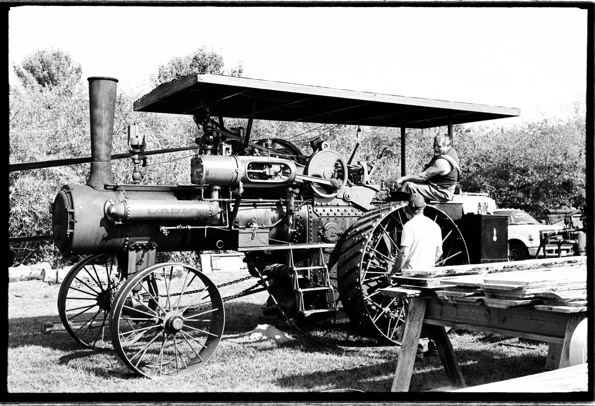 A black and white photograph of a vintage Case steam tractor driving a 56” saw mill at the Delaware Valley Old Time Power and Equipment Assoc. meet.