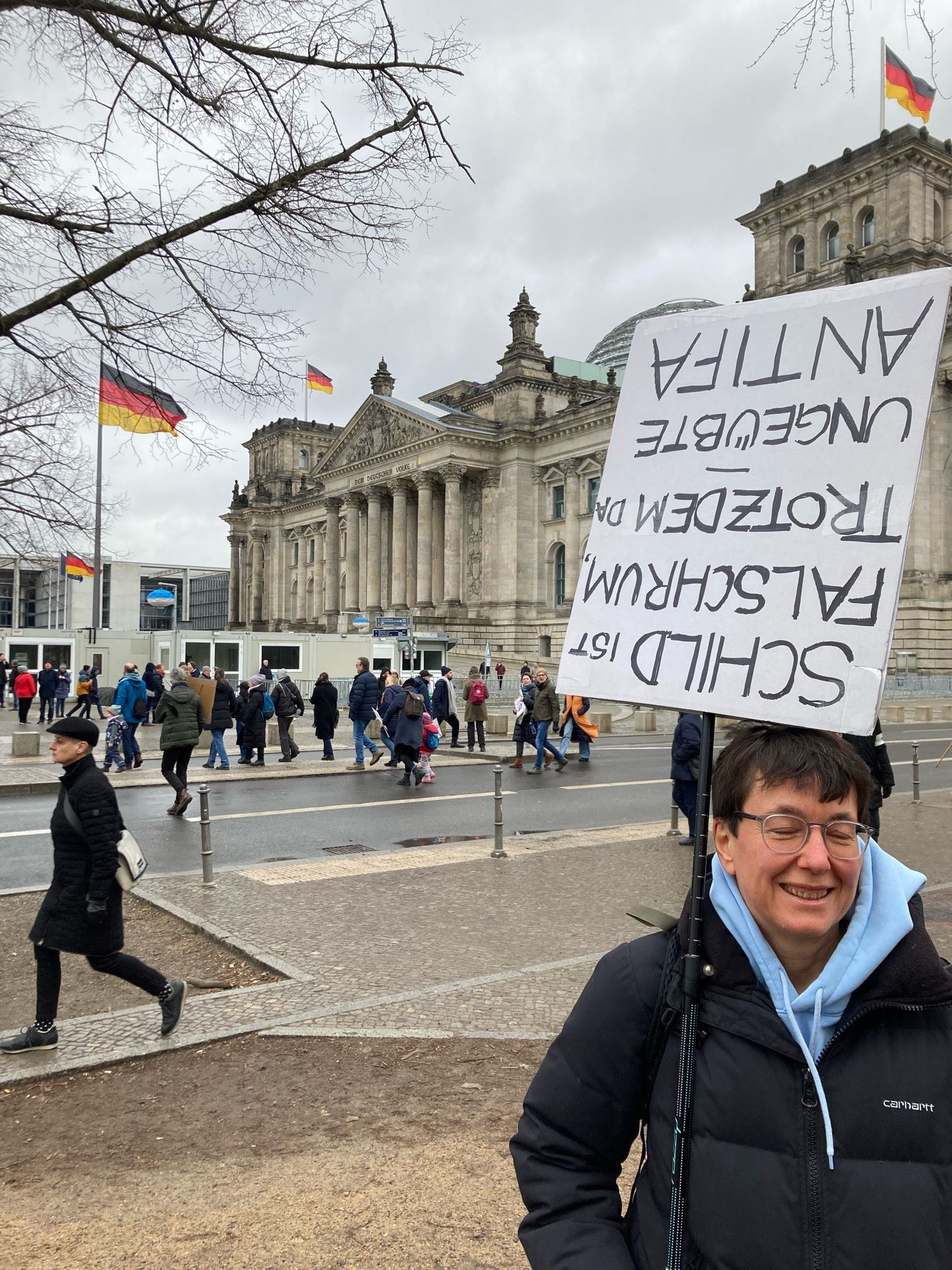 Kathrin hält ein Schild mit der Aufschrift „Schild ist falschrum trotzdem da ungeübte Antifa“ und steht vor dem Reichstag