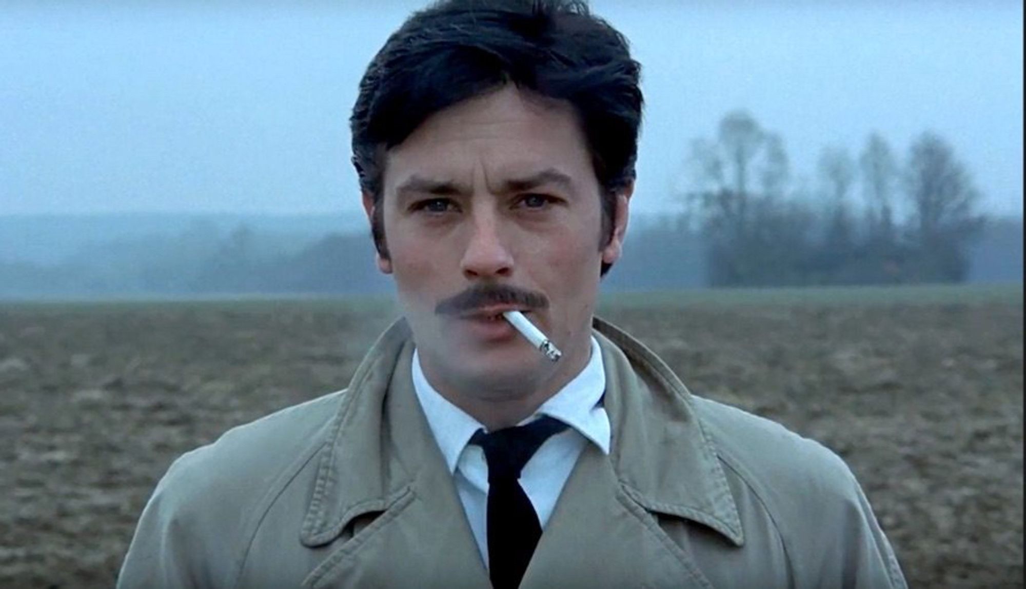 Alain Delon with a moustache and a fag hanging out of his mouth, in a field, in Le cercle rouge aka Red Circle.