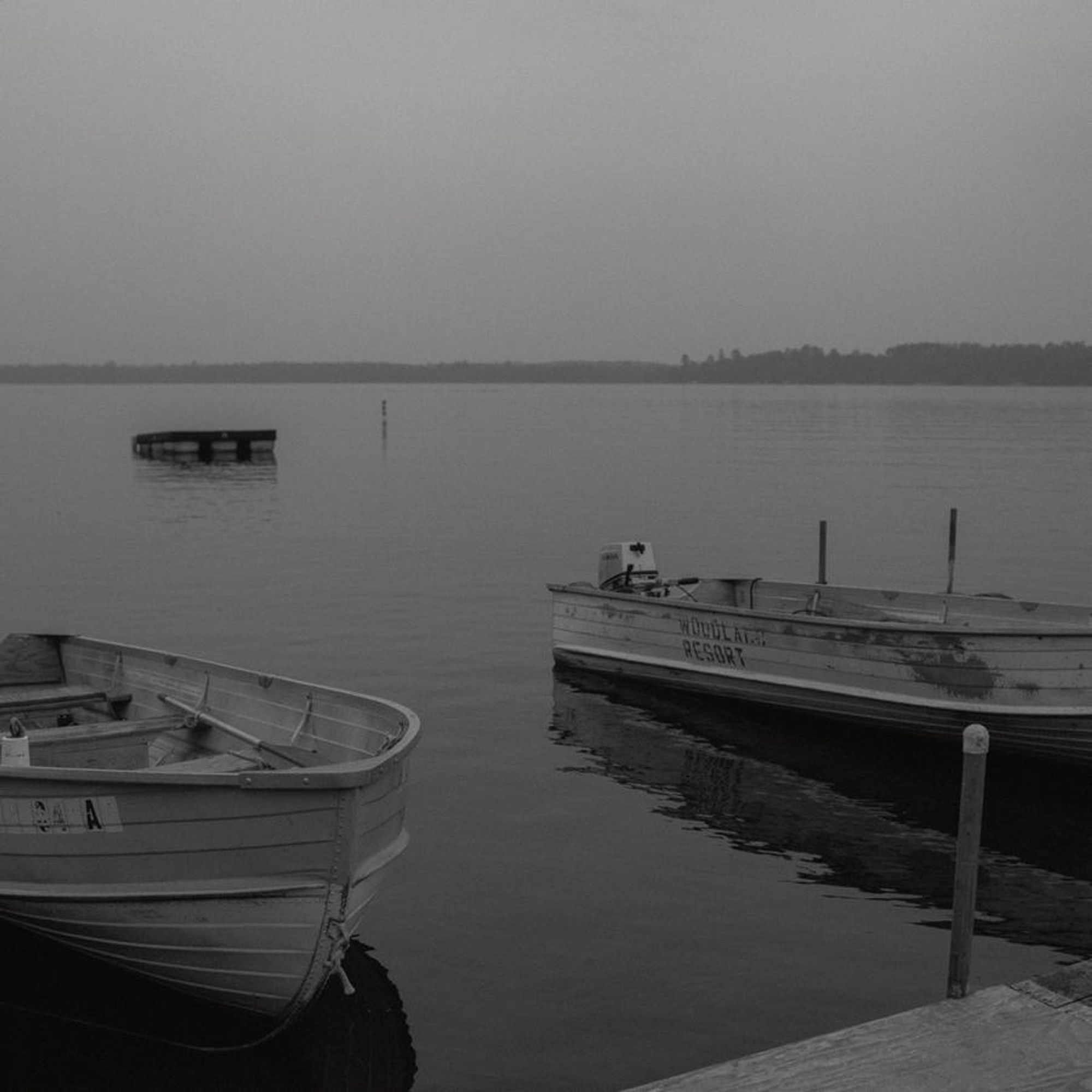 b&w photo of two boats tied up to a dock, behind them is an empty lake.