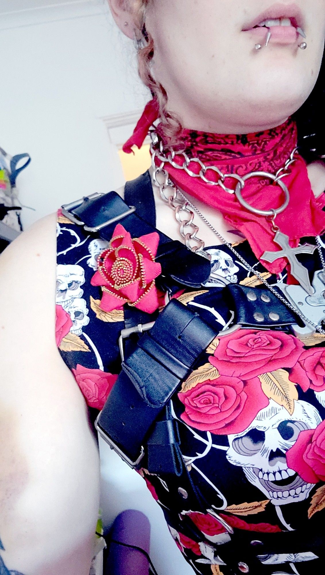 selfie of lilith wearing a red and black floral dress and a red bandanna with a flower made of half a zipper pinned to her chest harness on her right side