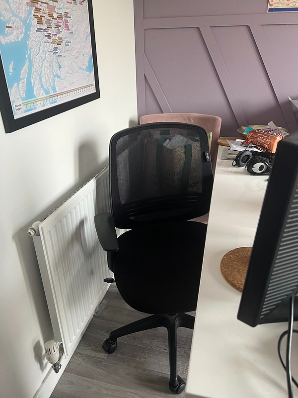 A comfy swivelly black office chair, with an uncomfortable kitchen chair now discarded behind it. There is a Munros wallchart above a radiator, and a tiny segment of a Euro 2024 wallchart.