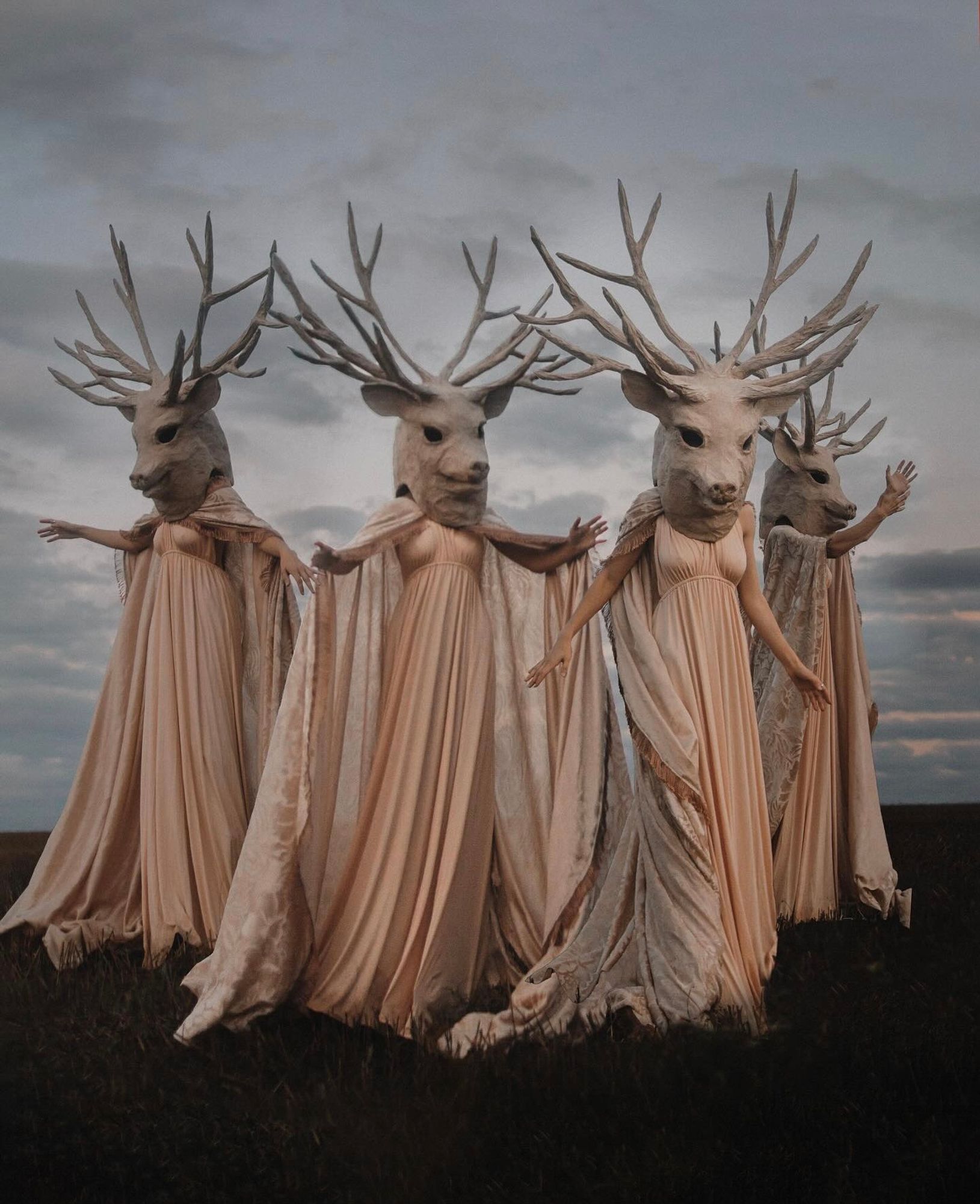 Photo of four female figures dressed in gowns and wearing animal heads with antlers.