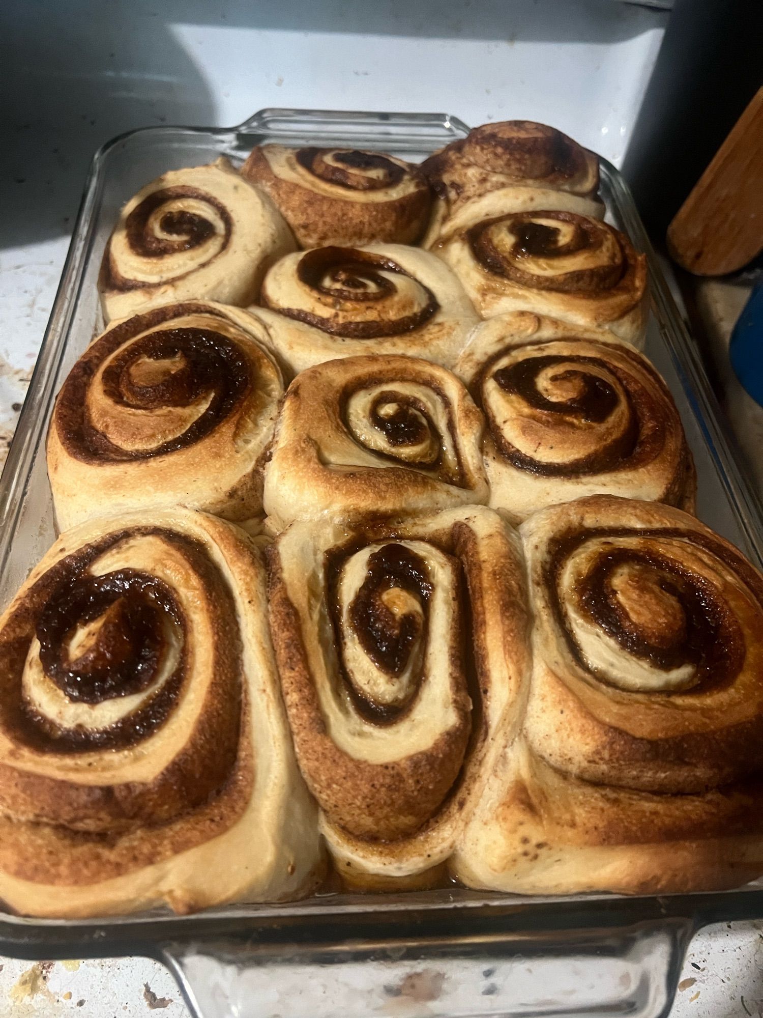 A full tray of unglazed cinnamon rolls, fresh from the oven, sitting on a stovetop.