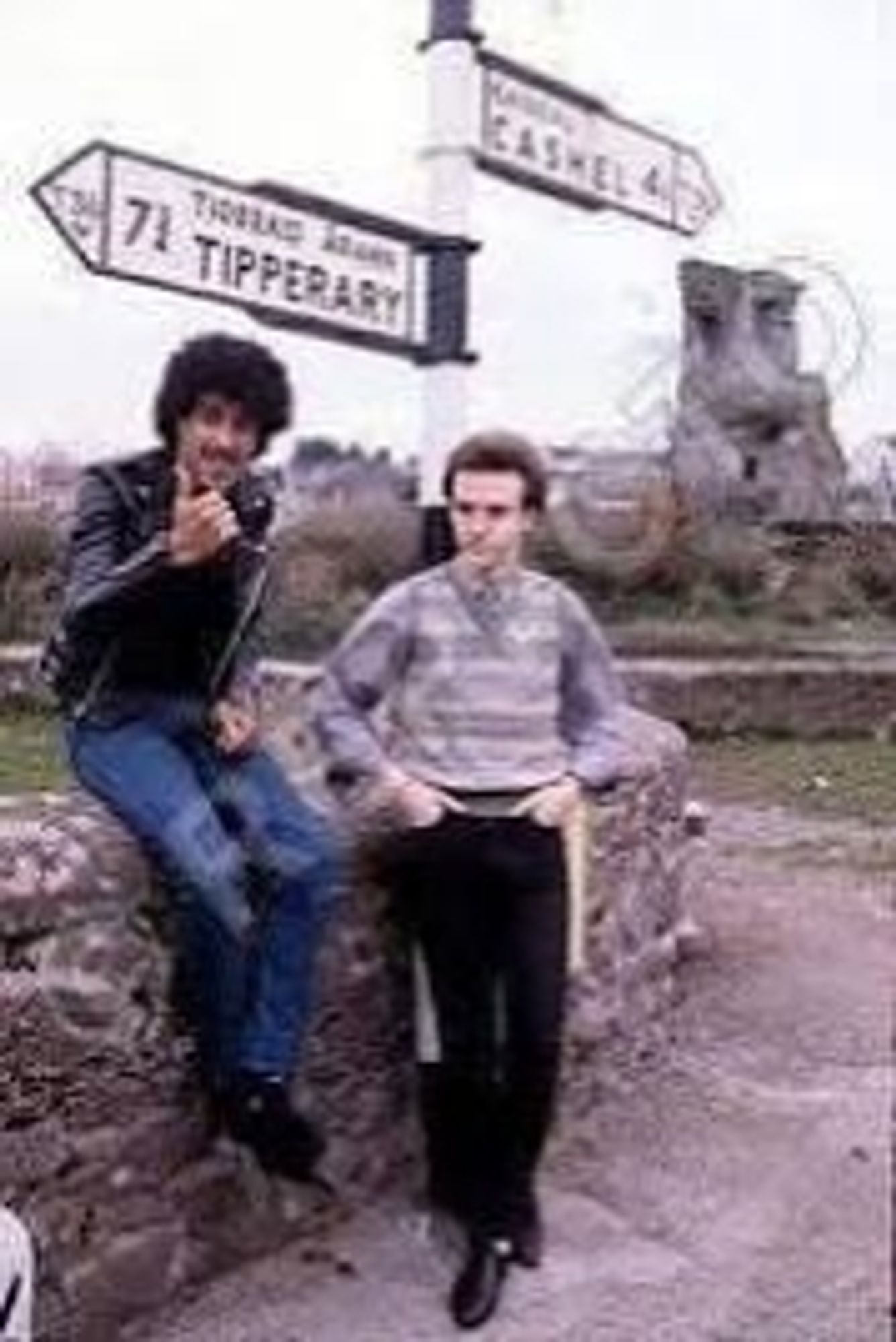 Phil Lynott and Midge Ure at a sign giving directions between Tipperary and Cashel