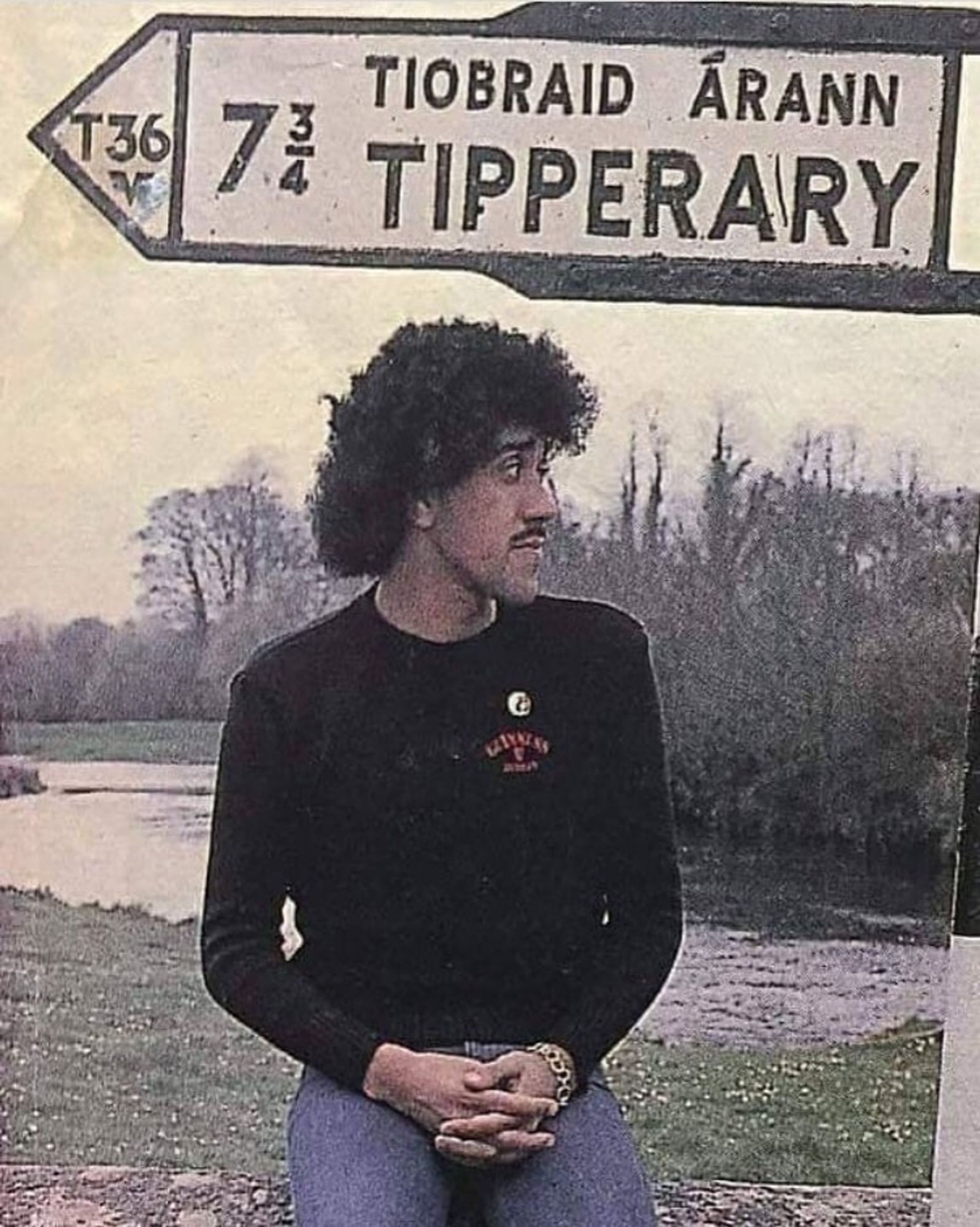 Phil Lynott under a sign giving directions to Tipperary