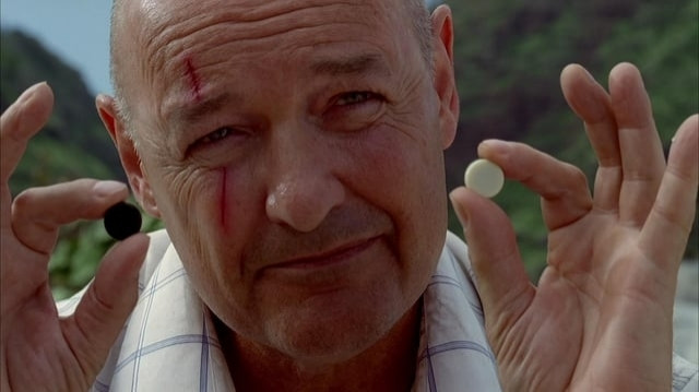 Foto do personagem John Locke, da série Lost, segurando duas pedras nas mãos e com o rosto machucado