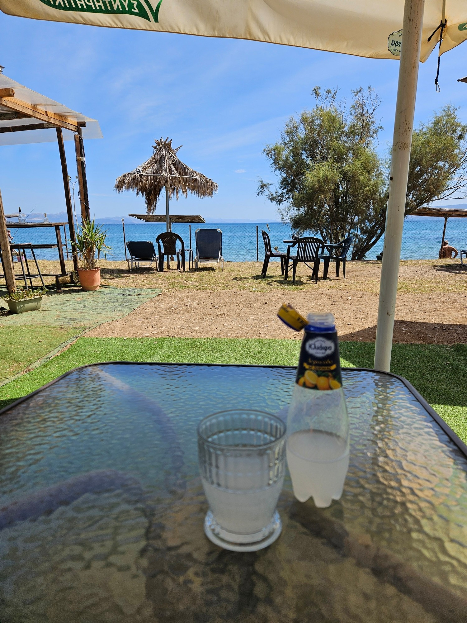 A table with a glass and a lemonade bottle, with a sea view in the background