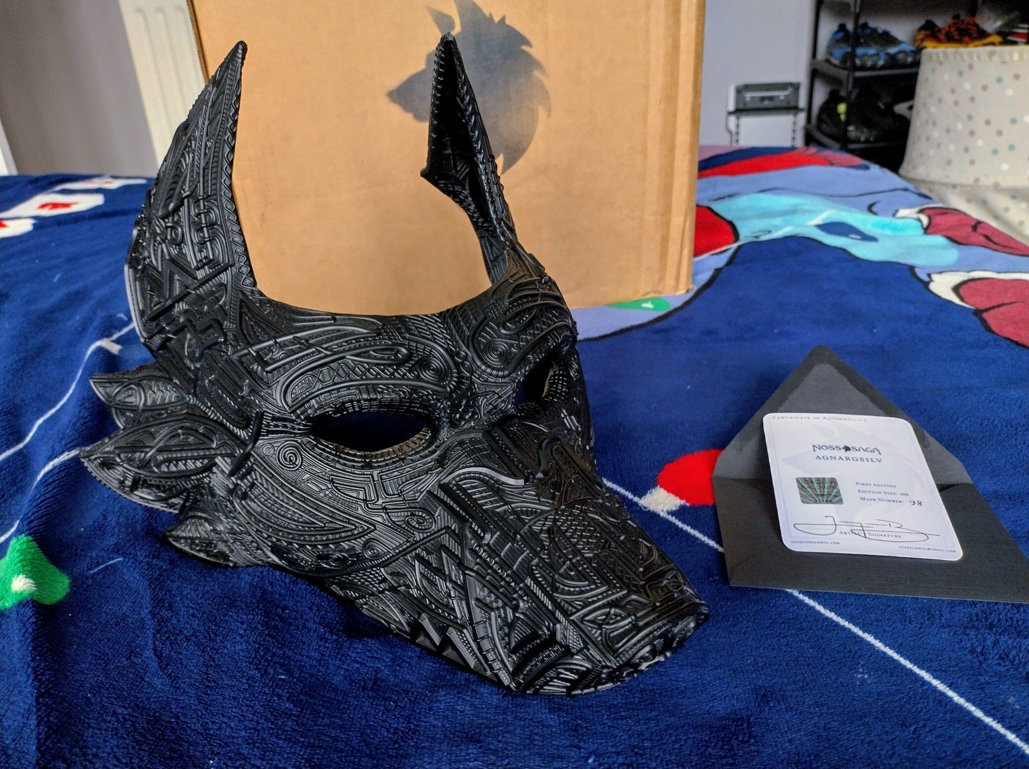 Agnargsilv, the canid mask from the Noss Saga sat on a bed next to its certificate of authenticity after having been unboxed.