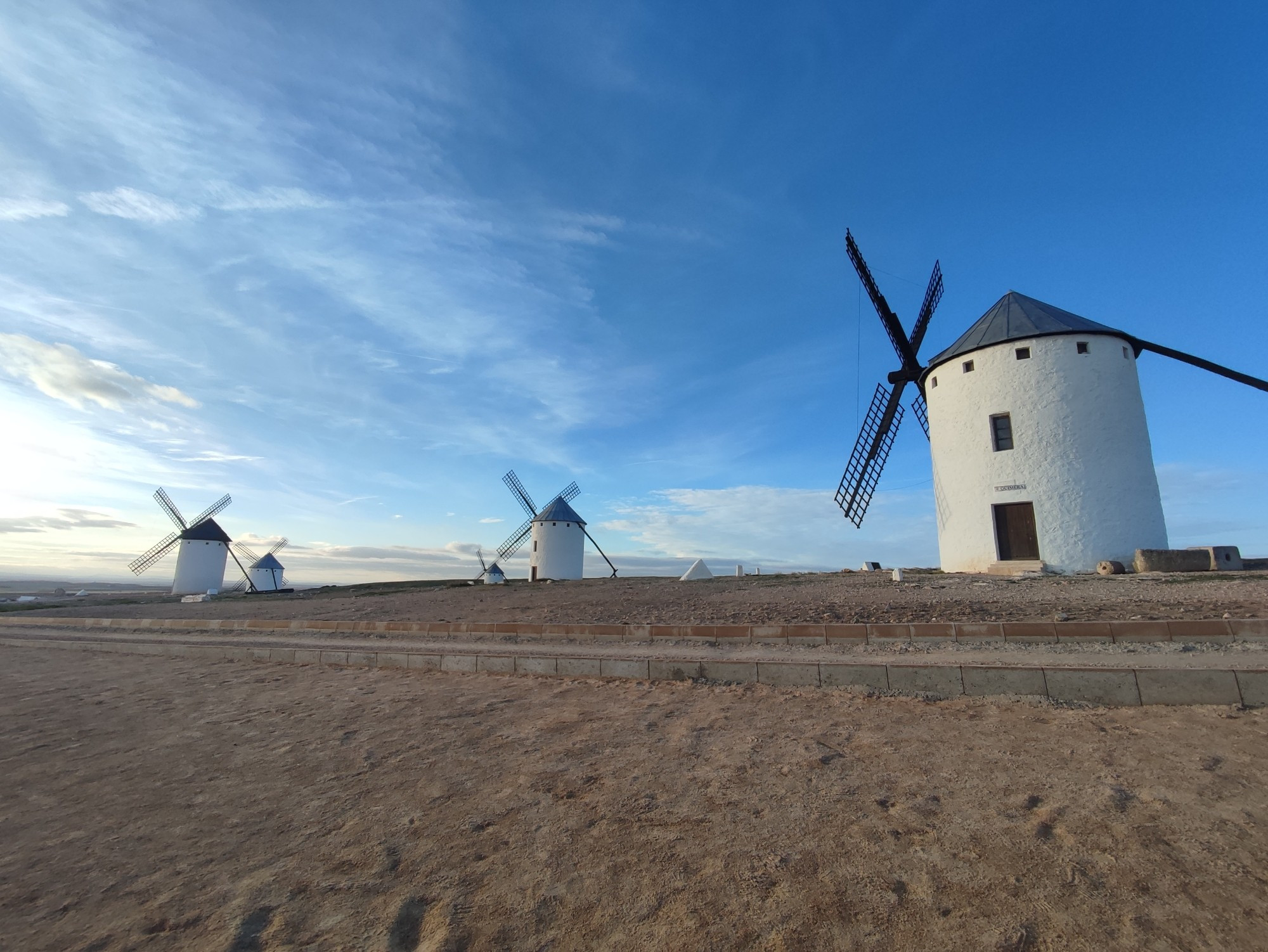 Una serie de molinos manchegos bajo un cielo azul con nubes.