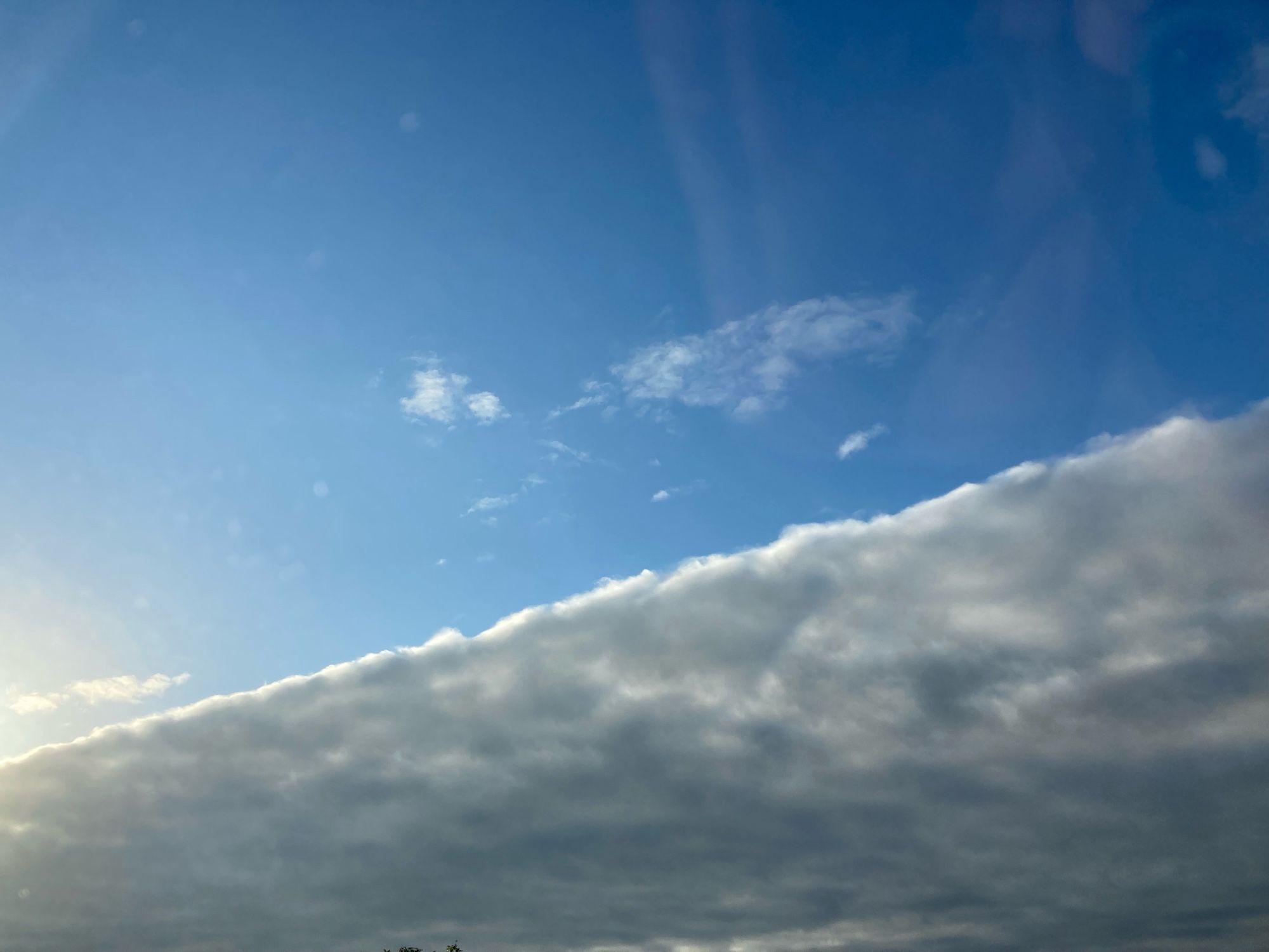 Der Morgenhimmel, diagonal geteilt in abziehende Wolken und Blau mit erstem Sonnenschein.