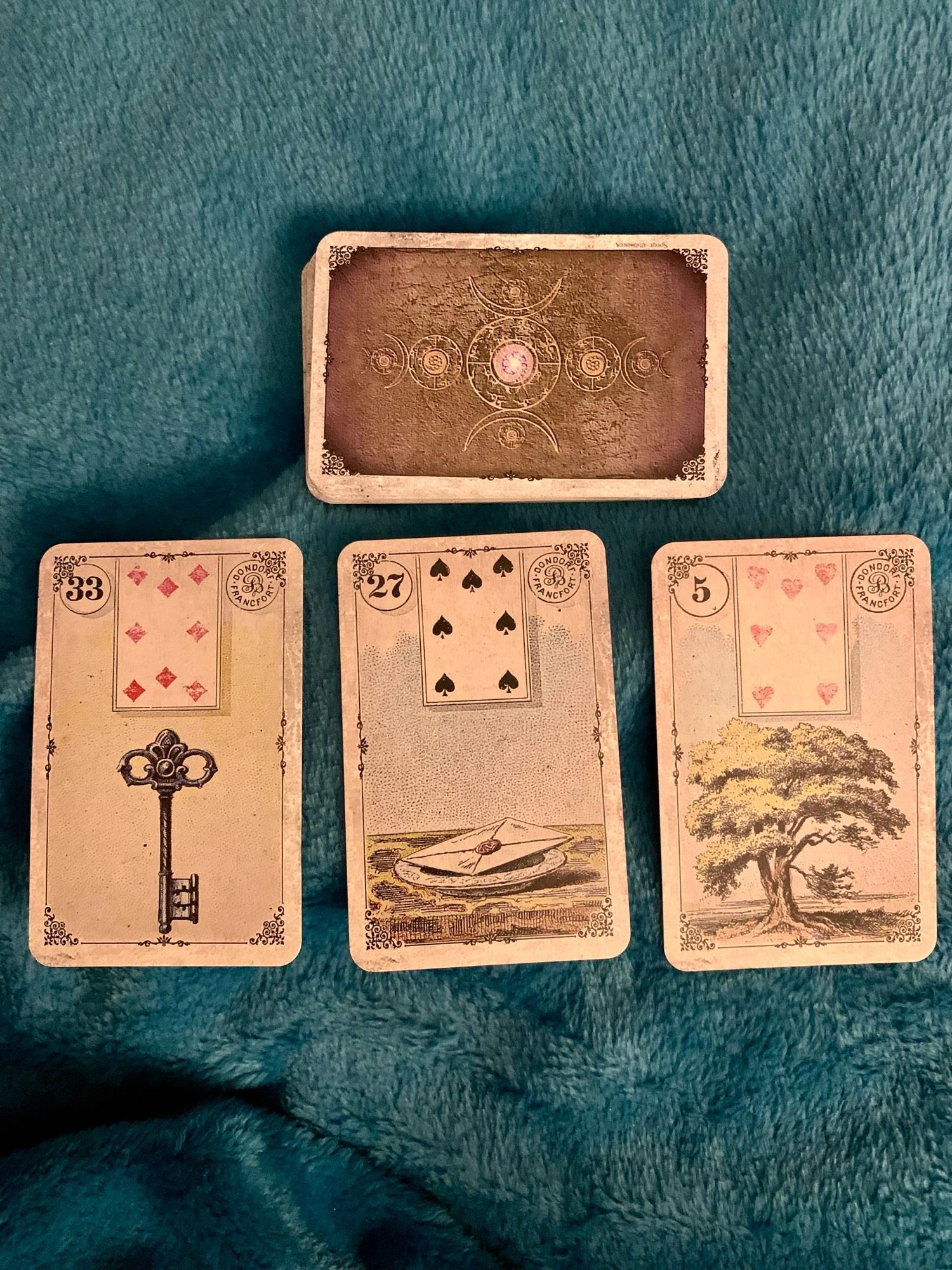 Photo of a pack of Lenormand divination cards on a dark teal background, with the Key, Letter, and Tree cards displayed. (From the Dondorf 1910 Lenormand reproduction.)