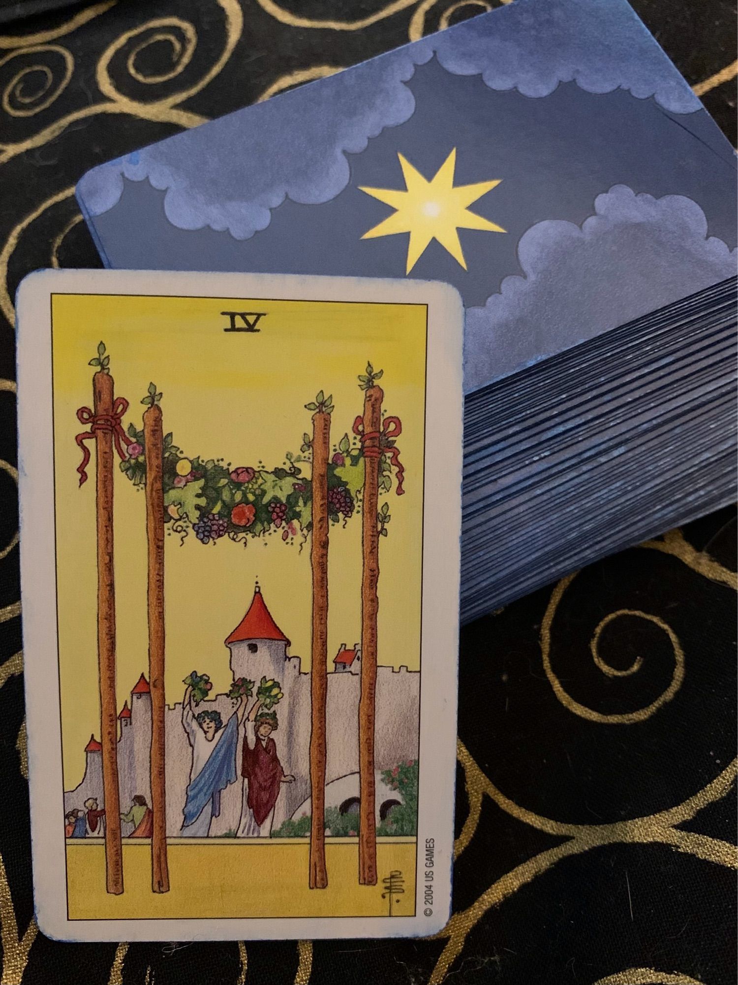 Photo of the Four of Wands from the Mini Universal Wait Tarot, propped against the remainder of the deck, on a black altar cloth with gold spirals.