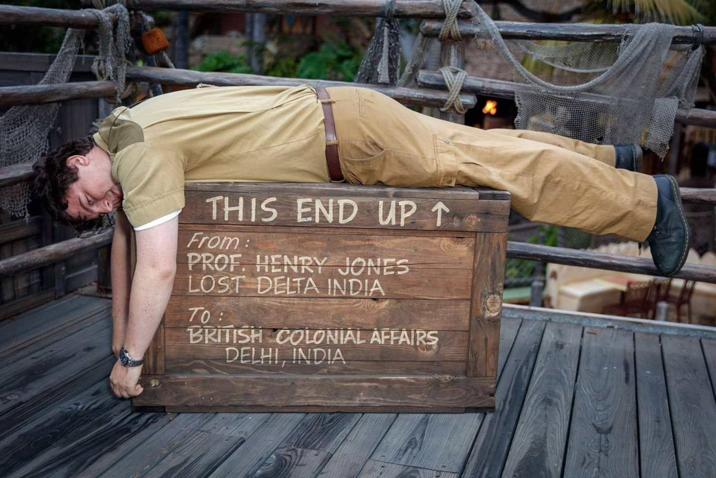 Me laying down stomach-first on a box while dressed in my Jungle Cruise outfit. My glasses are askew. The box says "this end up" and has an arrow pointing upward.