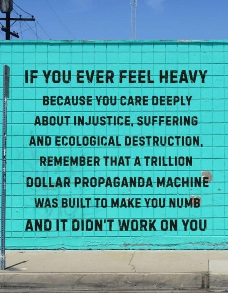 A picture of a wall with block letter graffiti reading:

If you ever feel heavy because you care deeply about injustice, suffering, and ecological destruction, remember that a trillion dollar propaganda machine was built to make you numb and it didn't work on you.