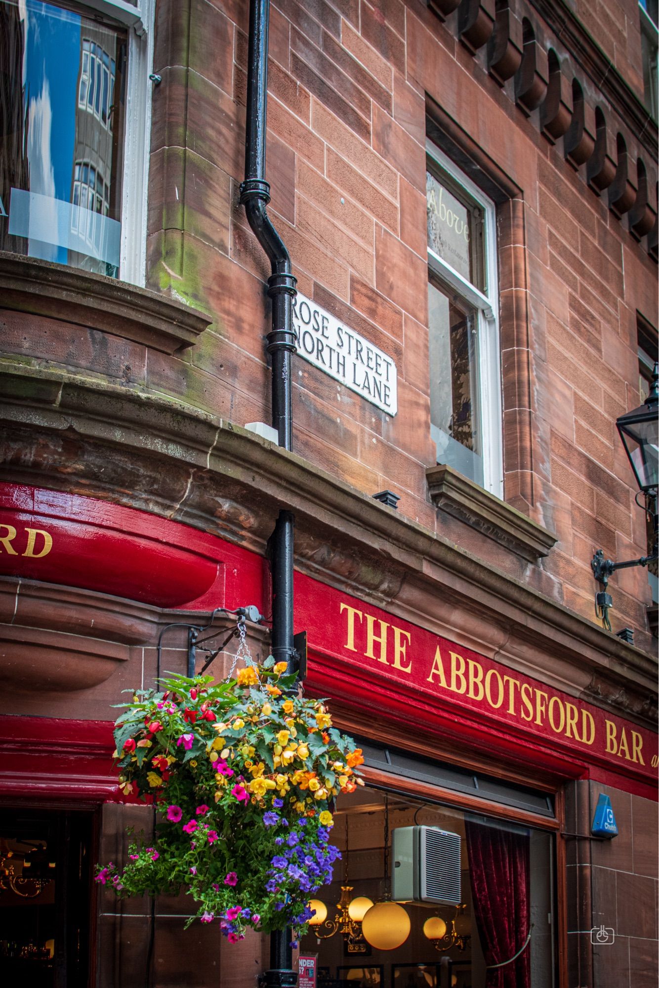 Colorful façade of a pub hung with bright flowers. Rose Street, New Town, Edinburgh, 22 Aug 2024. Nikon D5600, Nikkor DX 35 mm ƒ1.8G, ISO 800, ƒ4, -0.3 ev, 1/80s, polarizing filter