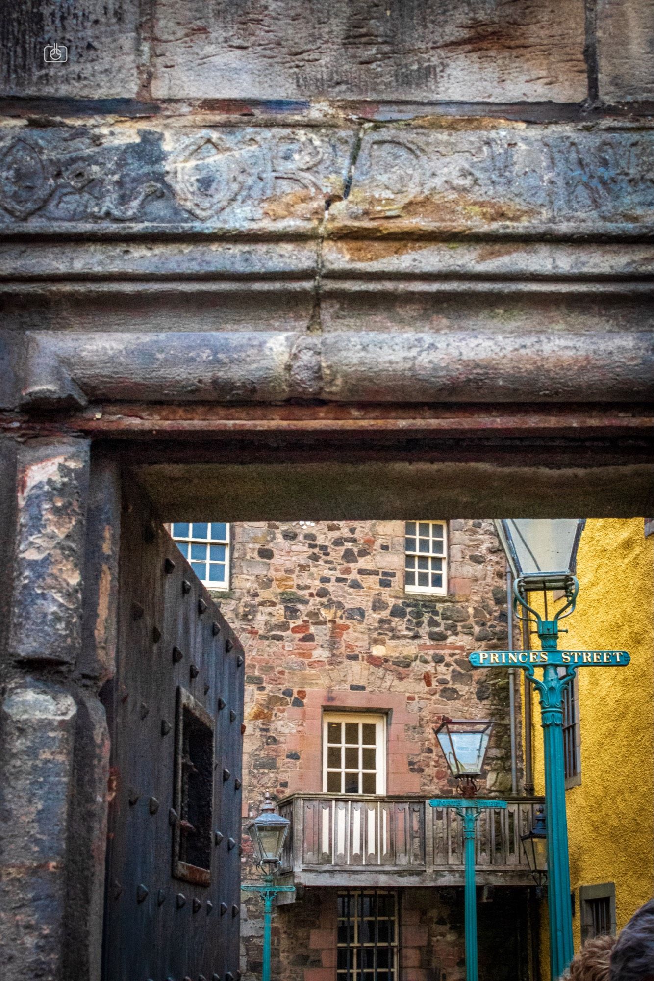 A stone gate with the words “O LORD” carved into the lintel, beyond which is a courtyard with old disused and partially broken street lamps and a wall painted bright yellow. Bakehouse Close, Canongate, Edinburgh, 19 Aug 2024. Nikon D5600, Nikkor DX 35 mm ƒ1.8G, ISO 3200, ƒ16, -0.3 ev, 1/60s, polarizing filter