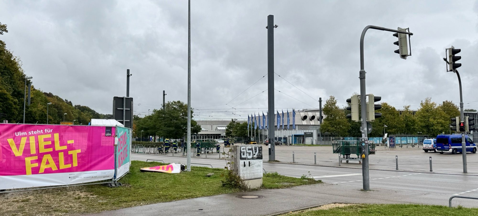 Links sieht man den Bauzaun mit den Planen
rechts den Eingang Messe Ulm
Davor baut das THW Gitter auf. 
Es ist der Fußgängerüberweg vom Parkplatz zur Messe