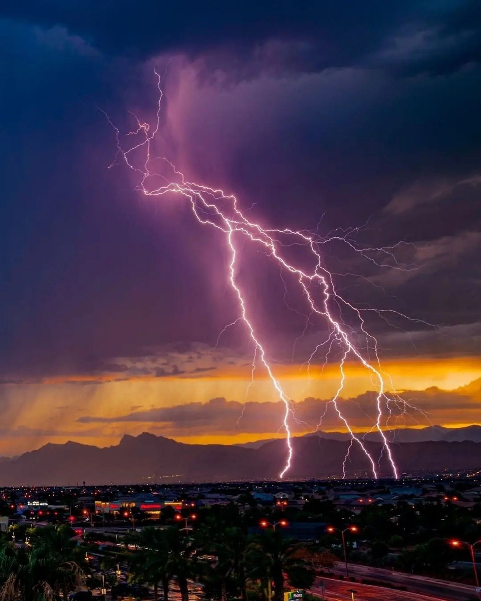 Pink colored monsoonal lightning striking over dusk Vegas Valley cityscape. Dark purple hills silhouetted in background, with golden sunset skies above, and matching purple monsoon storm clouds at top of frame. 

Photo credit: Shane Monahan (IG:@702_photo)