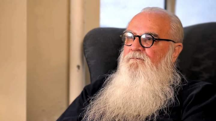 a man with glasses and a long white beard sitting in an armchair