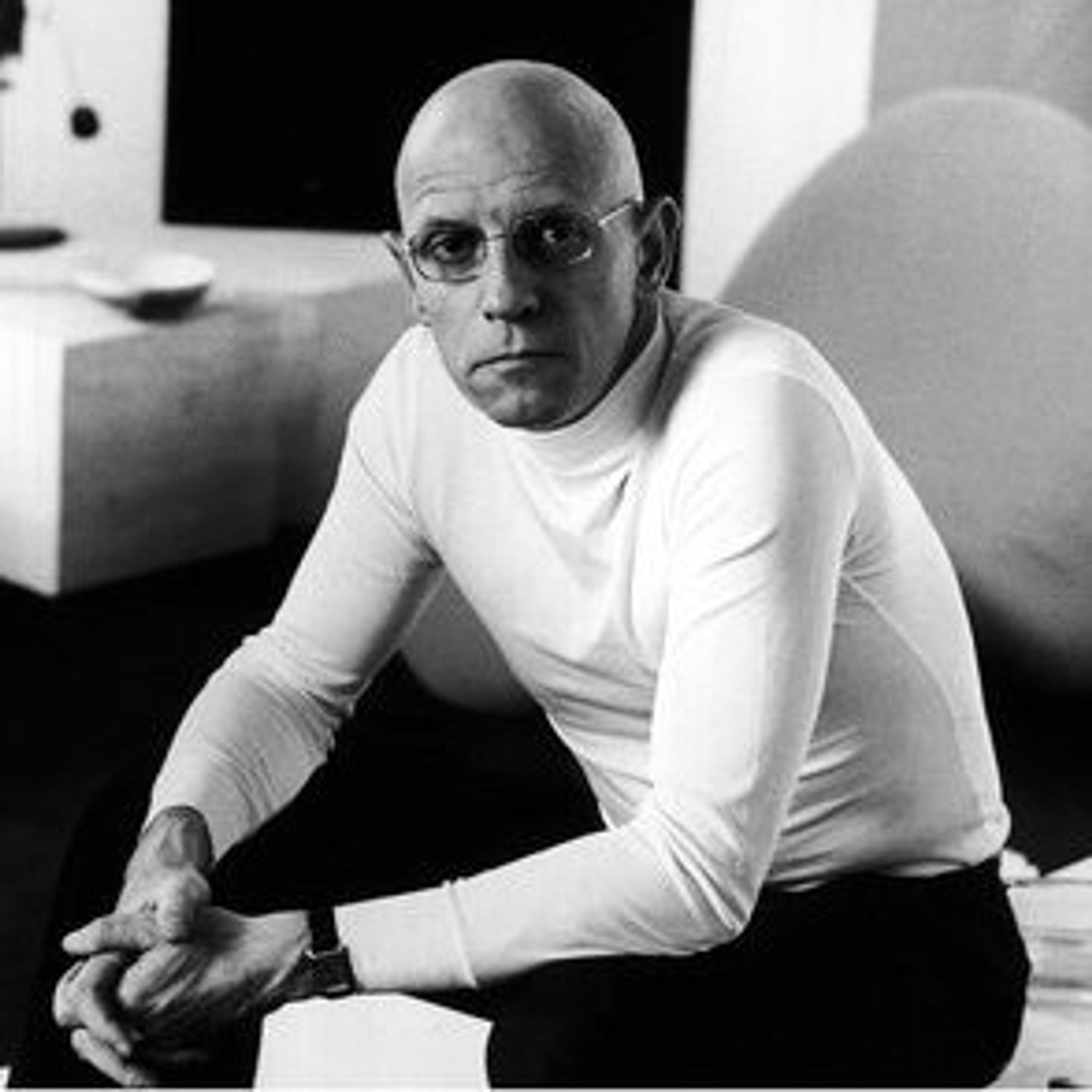 black and white photograph of Michel Foucault wearing a white turtleneck jumper and black trousers