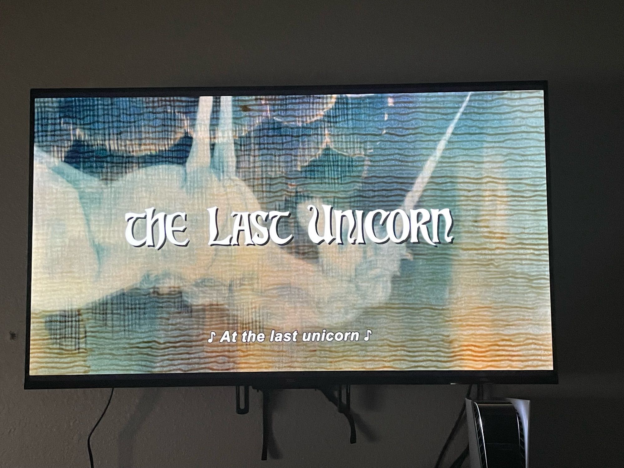 The title page of The Last Unicorn movie with song subtitles at the last unicorn and a tapestry style frame of a unicorn being reflected in water