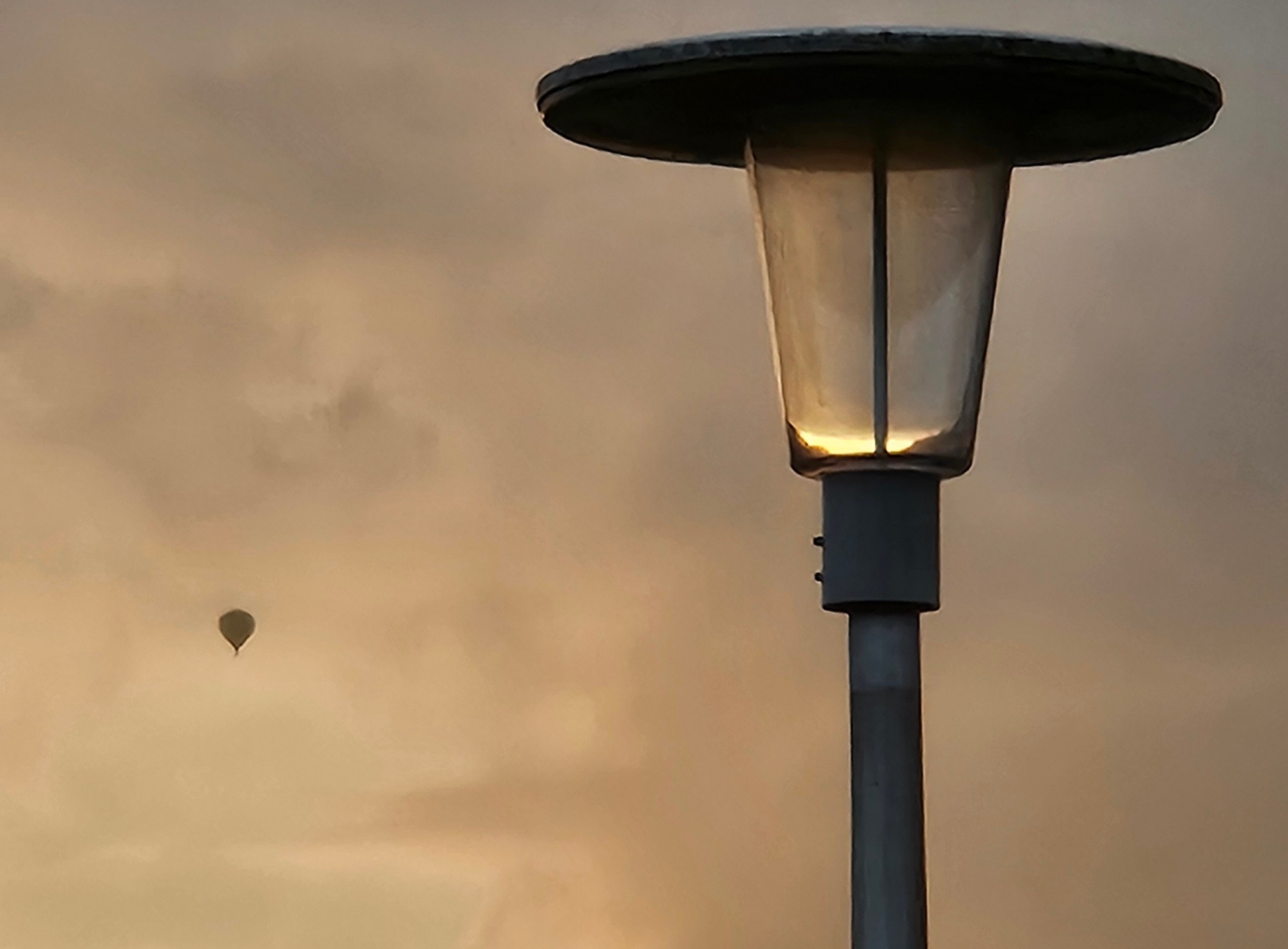 Luchtballon nadert - optisch - een straatlantaarn in goudgeel avondlicht