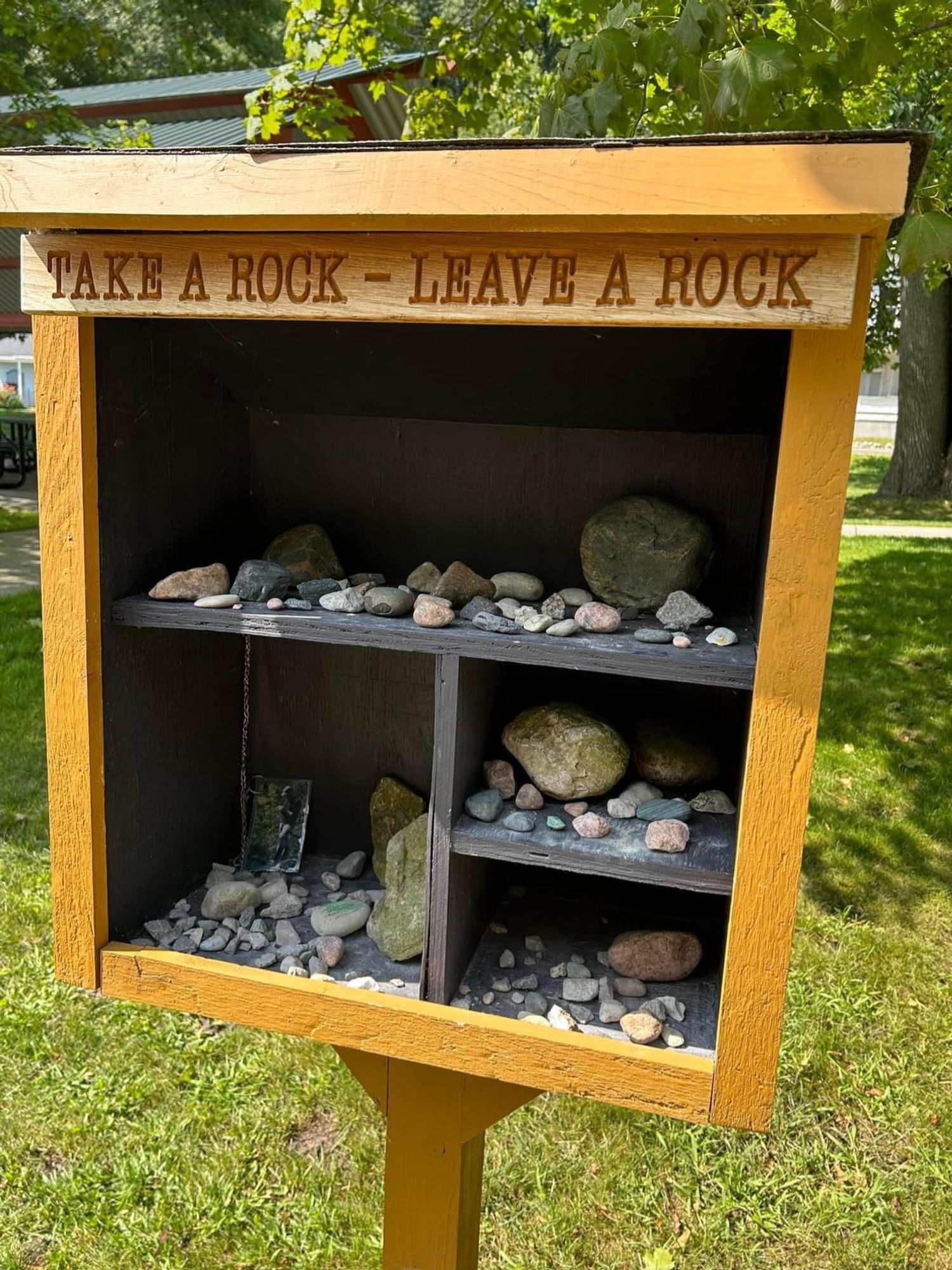 A wooden box on a post labeled "Take a rock - Leave a rock" It is filled with an assortment of rocks.