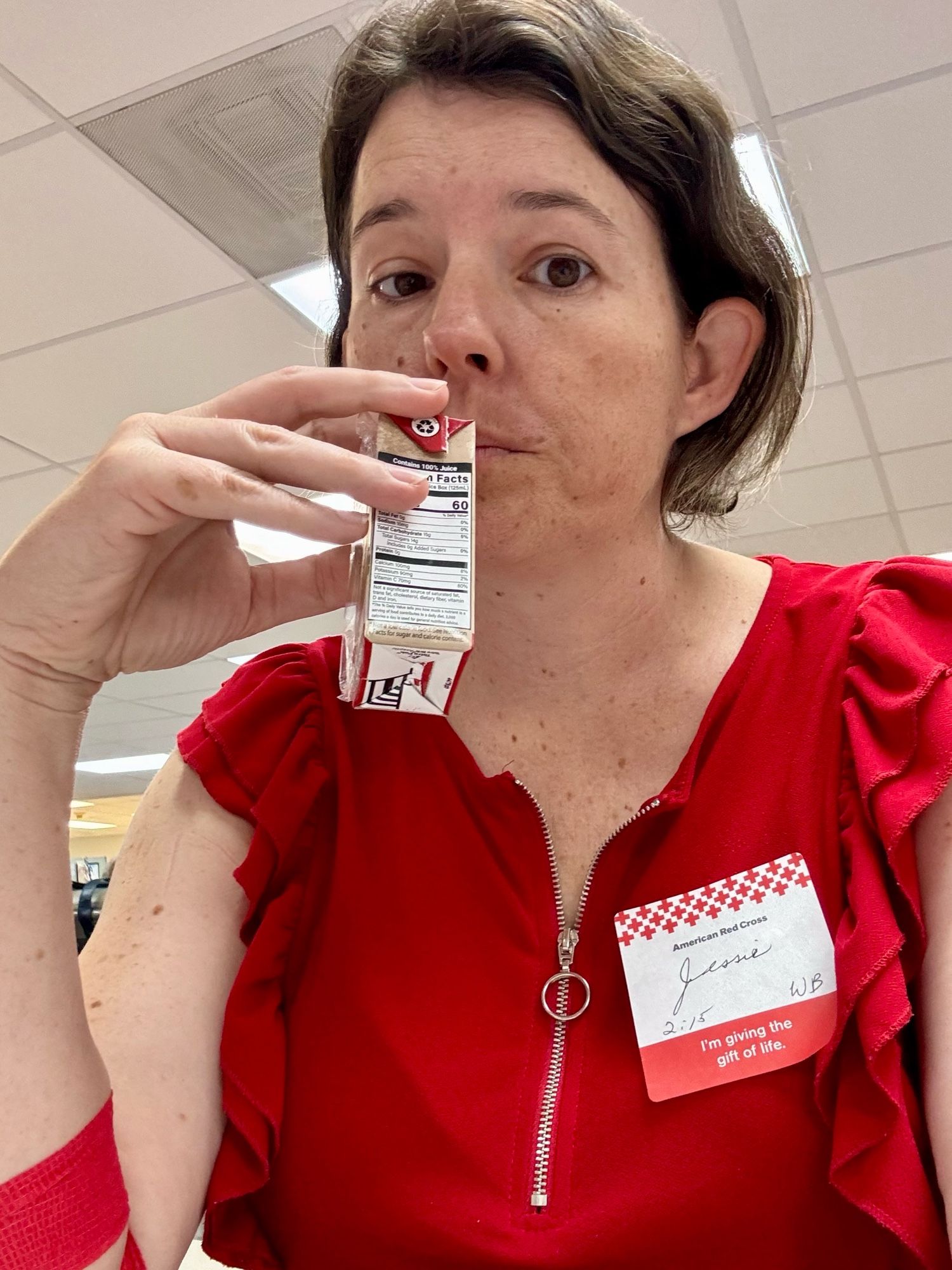 Selfie of Jessie in a red top with a blood donation sticker on, drinking a juice box.