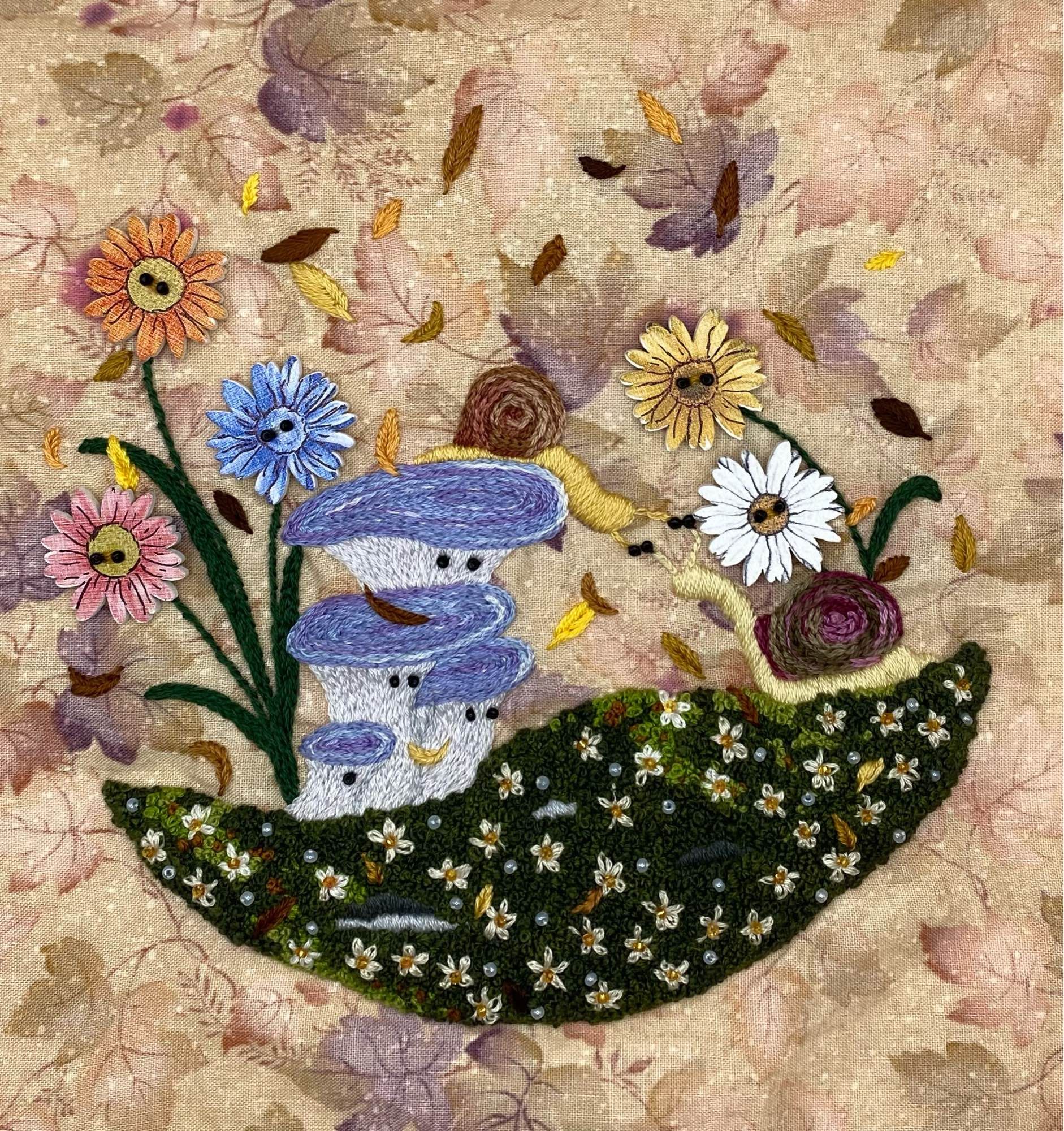 Multimedia embroidery with buttons and beads. Four blue oyster mushrooms watching two snails greet each other while some button daisies look on. Embroidered on brown, beige and purple cotton printed with autumn leaves.