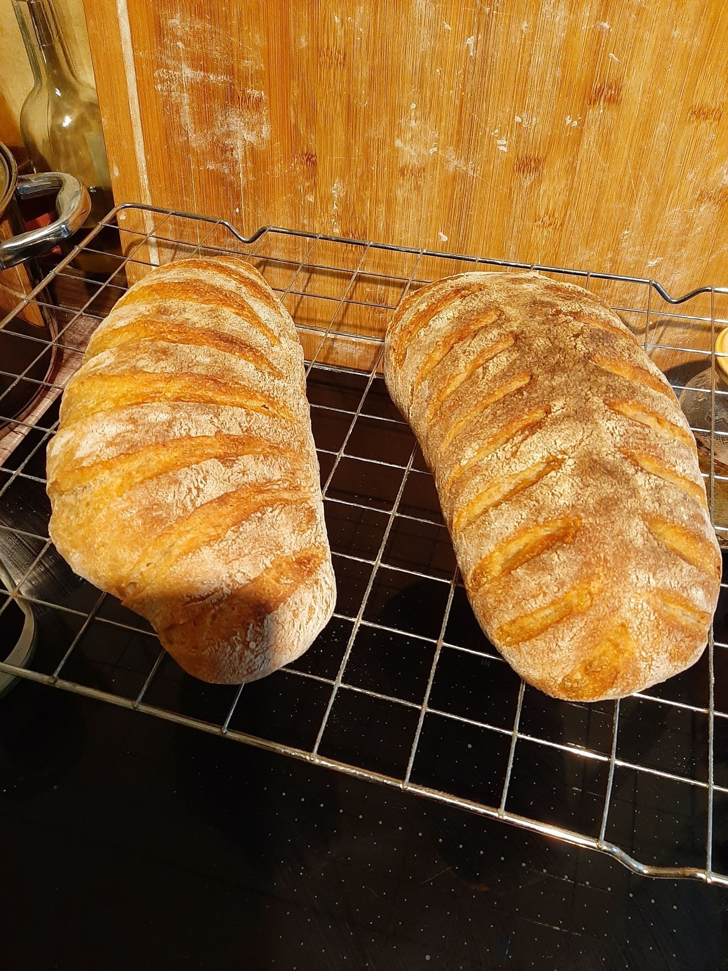 2 Laib Brot auf dem Abkühlgitter. Die Brote sind mit verschiedenen Mustern gestreift. Dahinter ein großes Holzbrett.