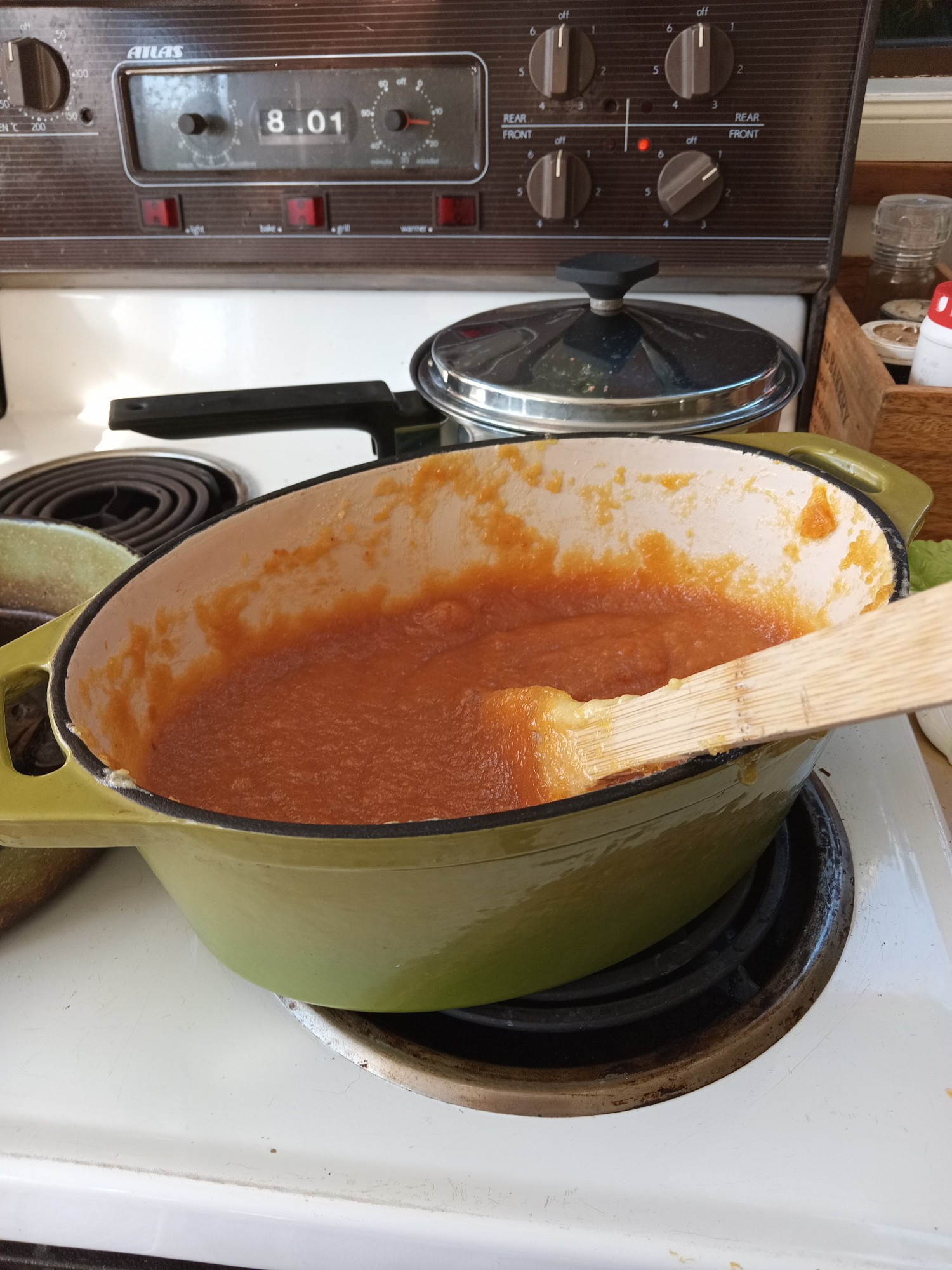 Amber coloured quince paste bubbling away in a cast iron casserole dish on a stove top element.