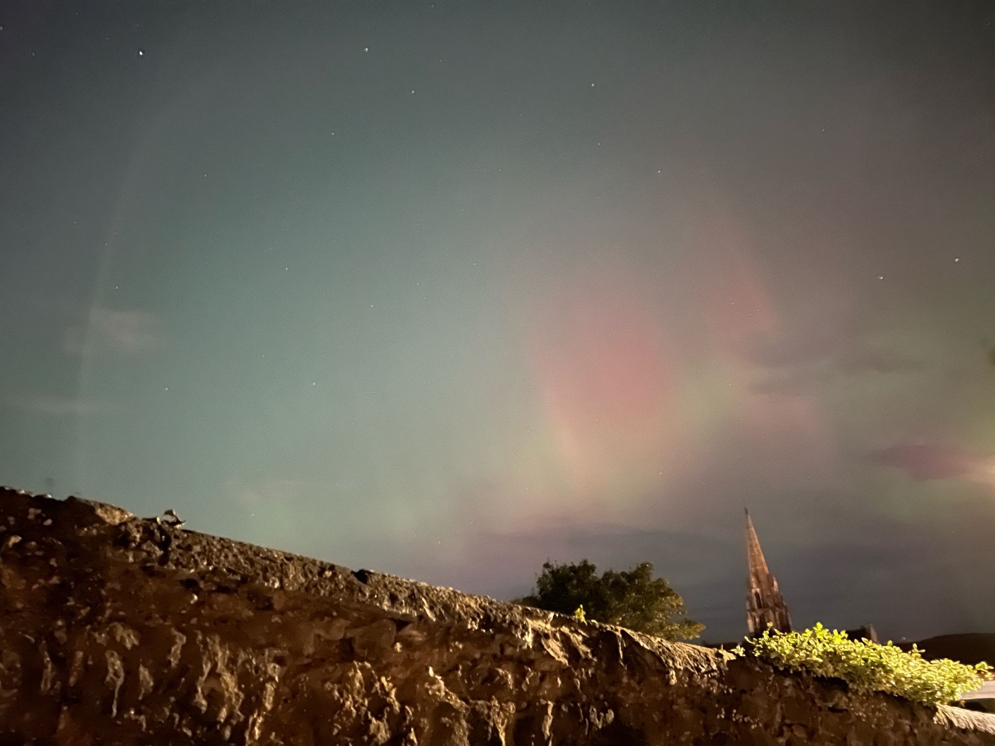 Looking over a stone wall, with a church steeple in the distance. Pink tinges from the Northern lights