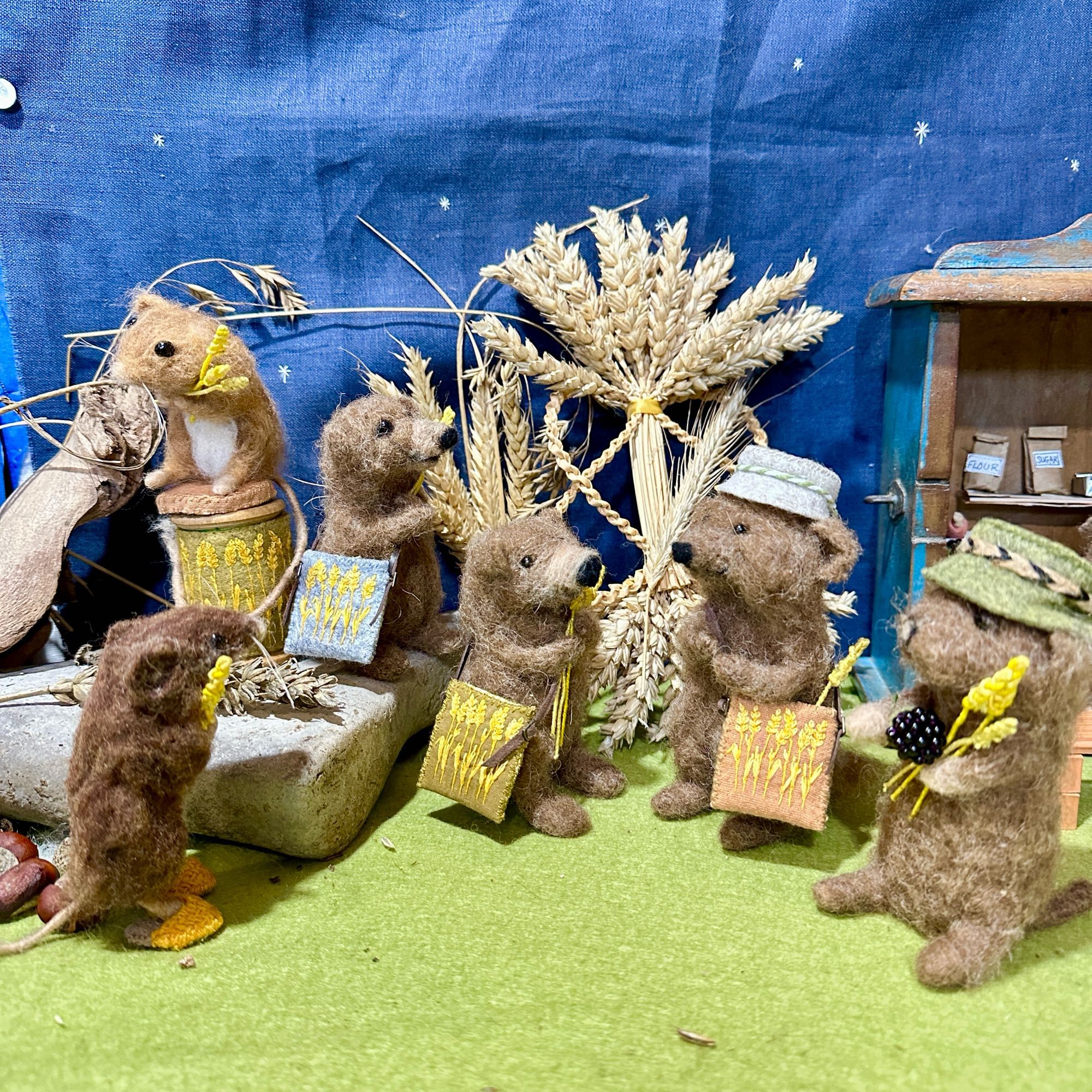 A group of needle felted animals with embroidered bags and hats and wheat stalks