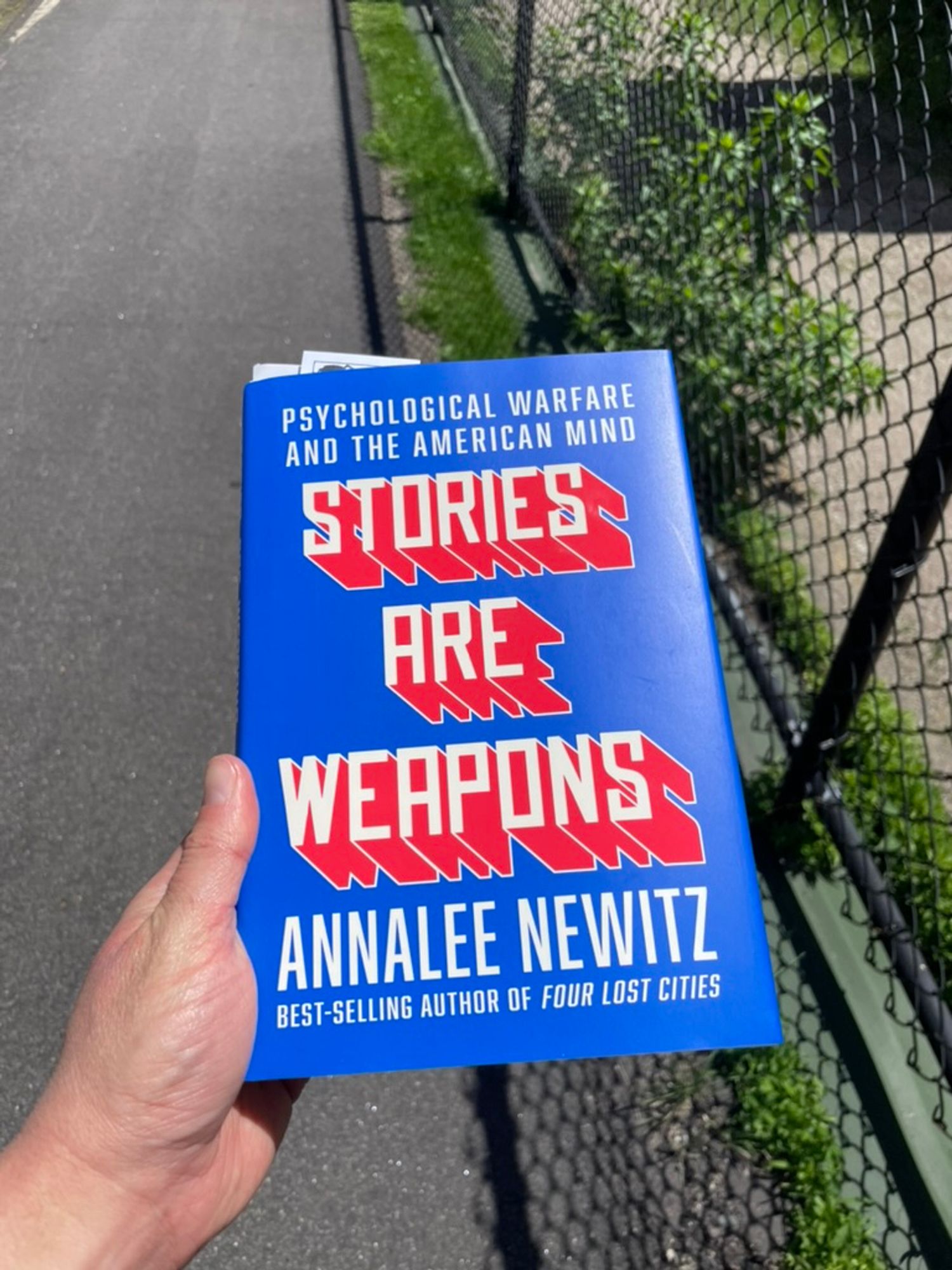 holding book outside: STORIES ARE WEAPONS: PSYCHOLOGICAL WARFARE AND THE AMERICAN MIND by Annalee Newitz