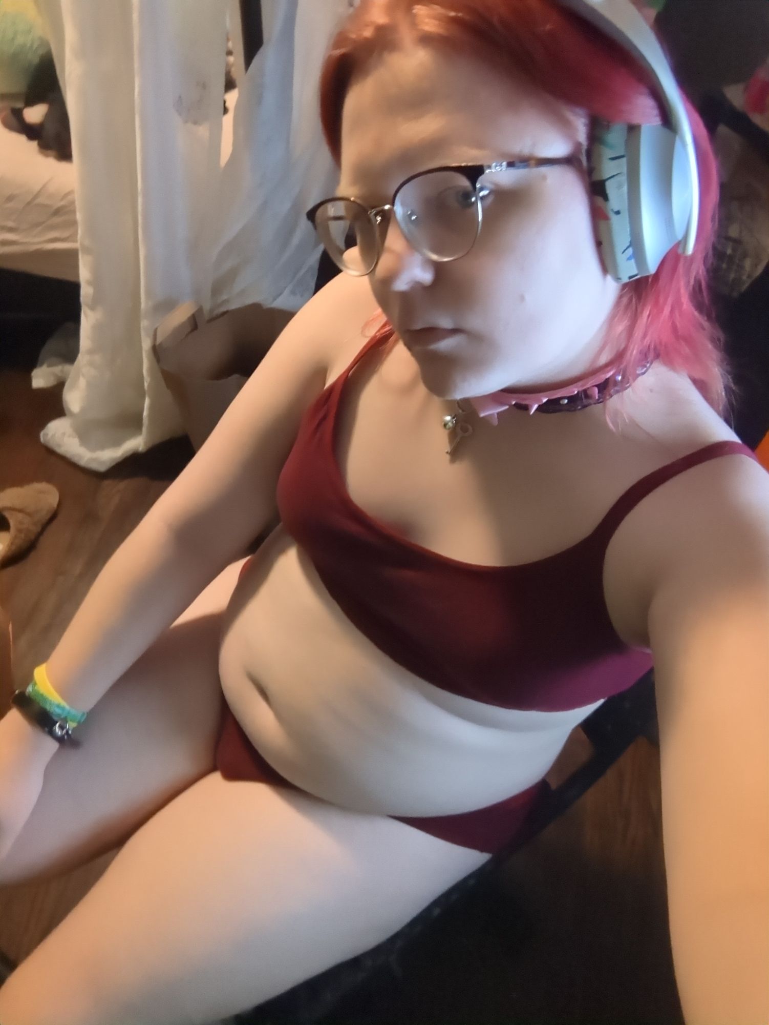 Many, wearing a spiked collar, red bra, and the same panties, in faer chair, bulge visible, chubby tummy all cute and prominent.