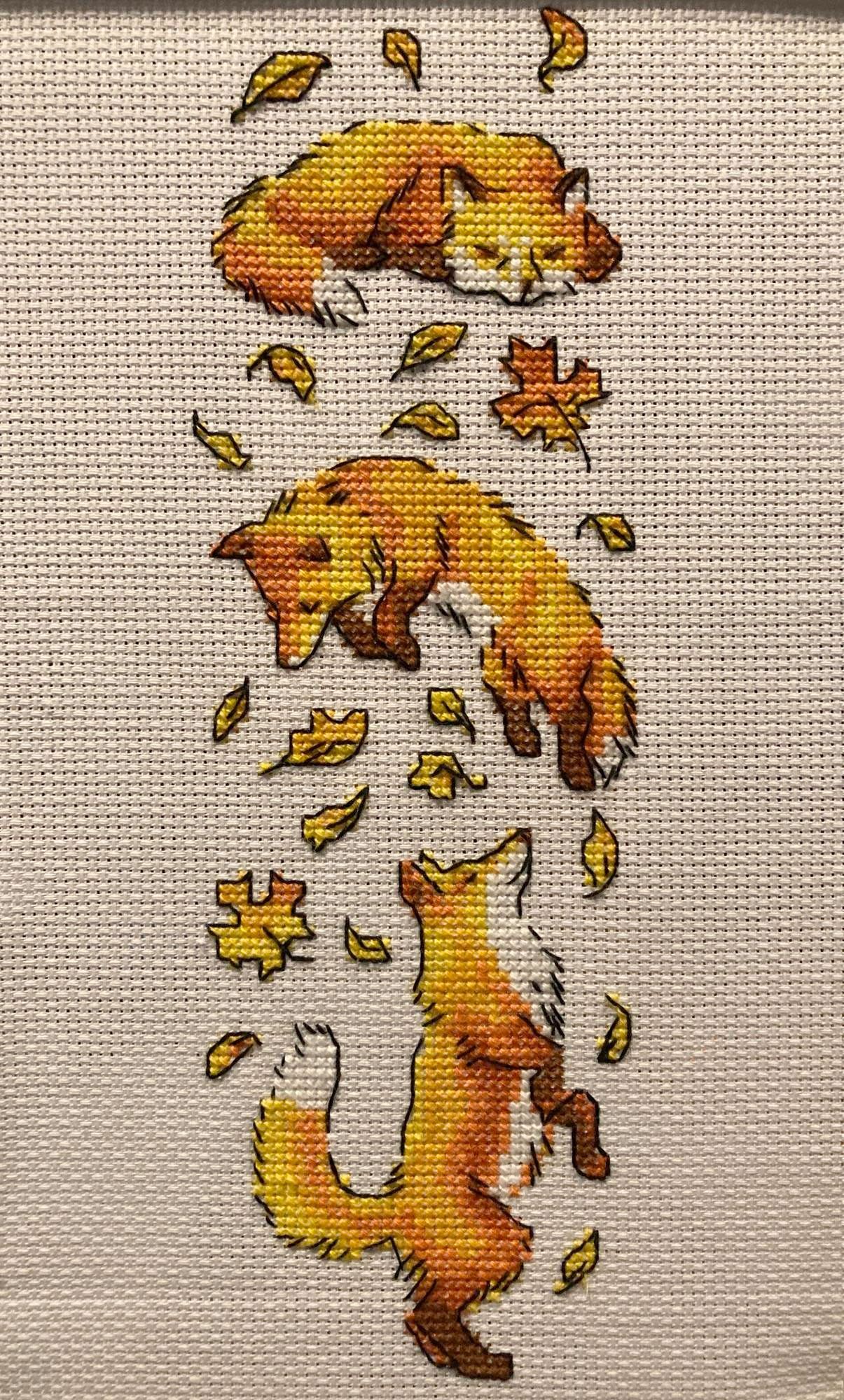 Cross stitch of three foxes playing in falling leaves. 