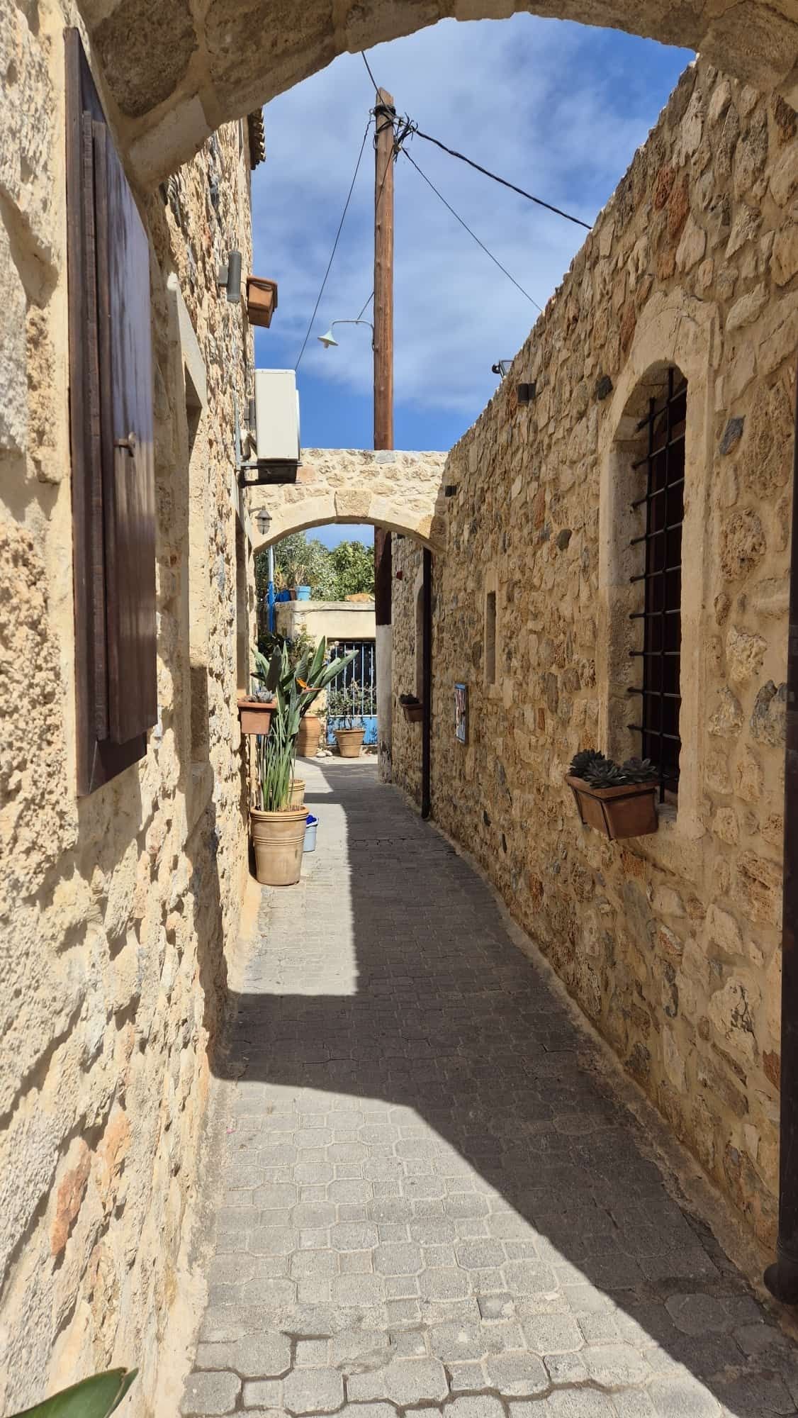 Blick in eine enge Gasse im Ort Chersonissos auf Kreta, in der gut getarnt überraschend eine Katze aufgetaucht ist.