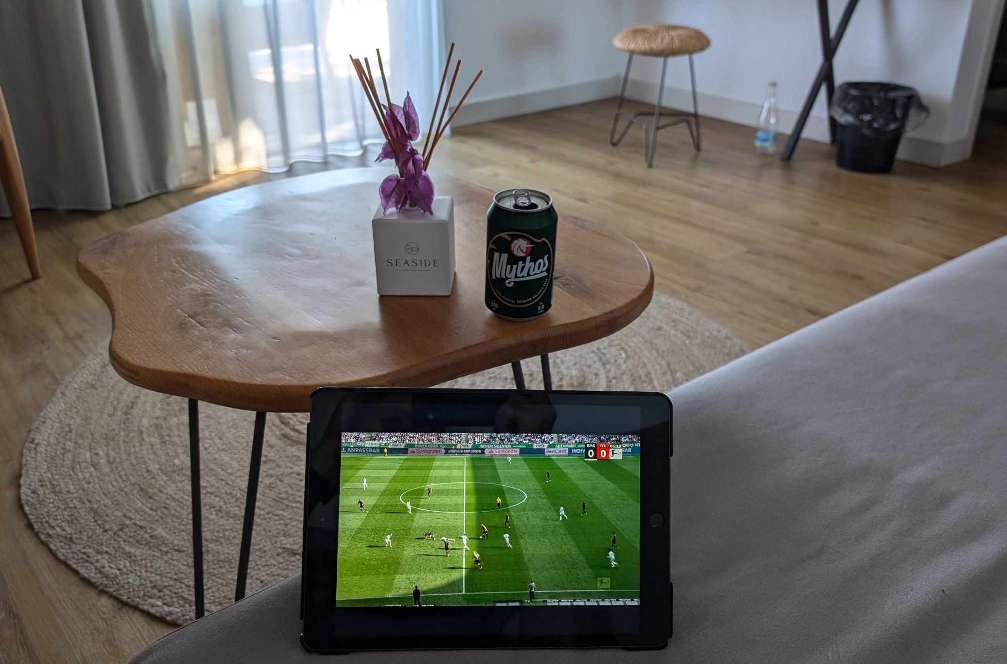 SkyGo zeigt die Partie auf meinem iPad. Hinter dem iPad stehen auf einem runden Holztisch eine Dose Mythos Bier und Duftstäbchen des Seaside Hotels.