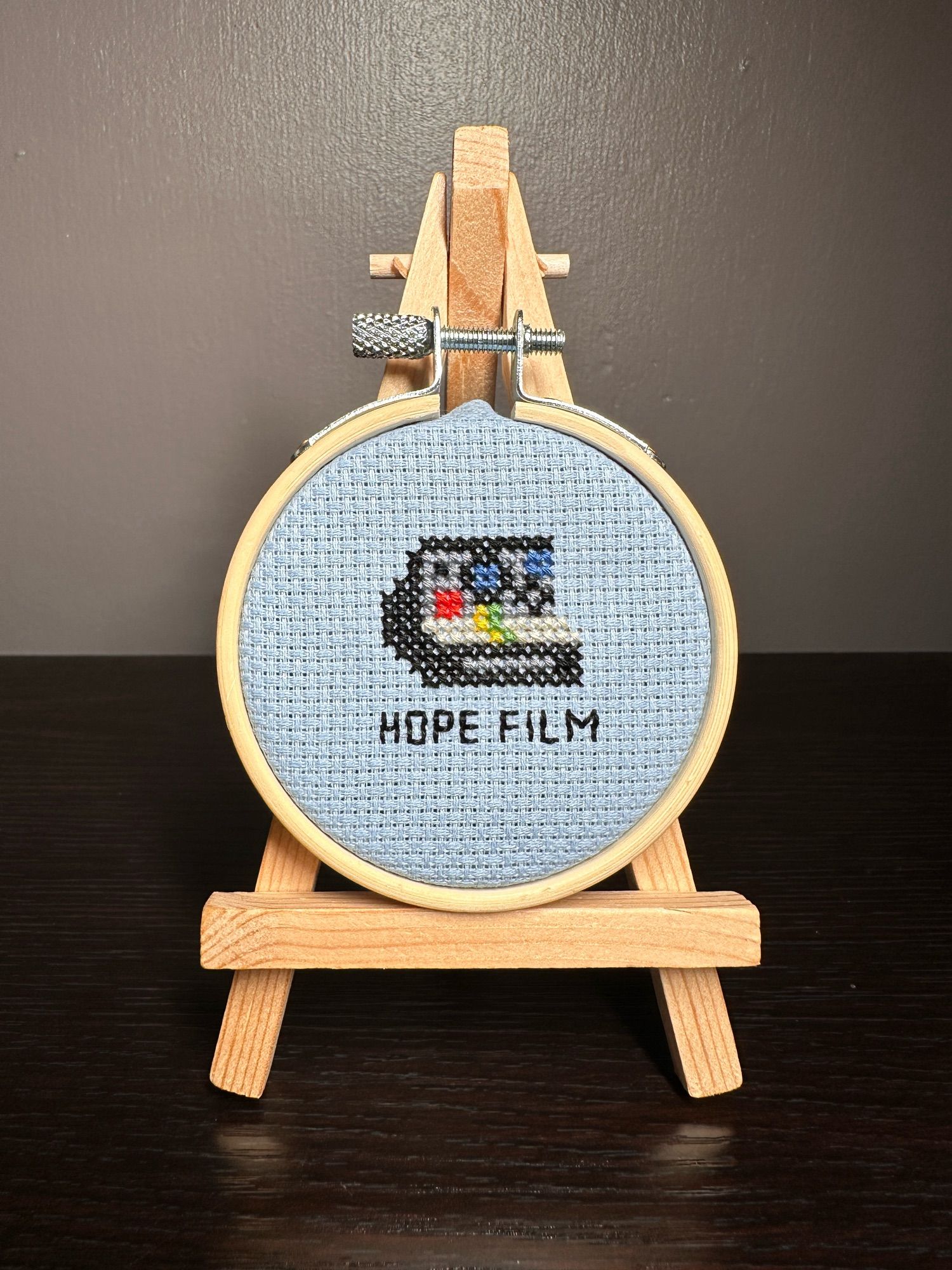 a tiny cross stitch of a Polaroid camera with the text “hope film” underneath