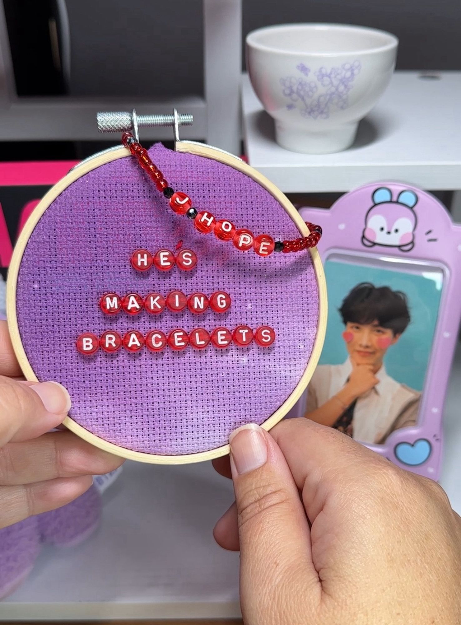 an embroidery hoop with red alphabet beads saying “he’s making bracelets”