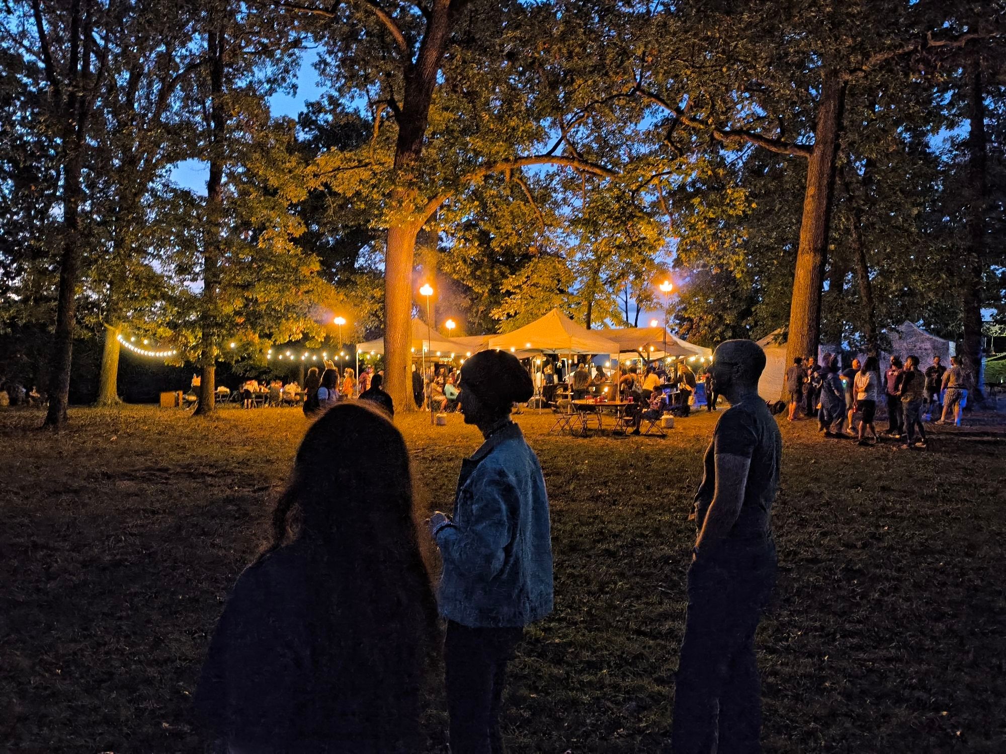 A sunset pic of 3 people playing bocci, a well lit outdoor bar in the background.