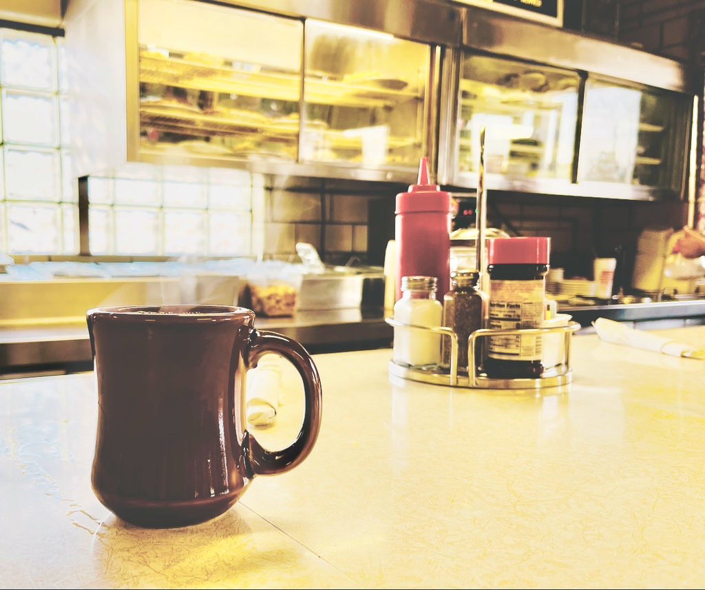 photo of diner coffee mug on counter with ketchup, salt shaker, and traditional diner backdrop