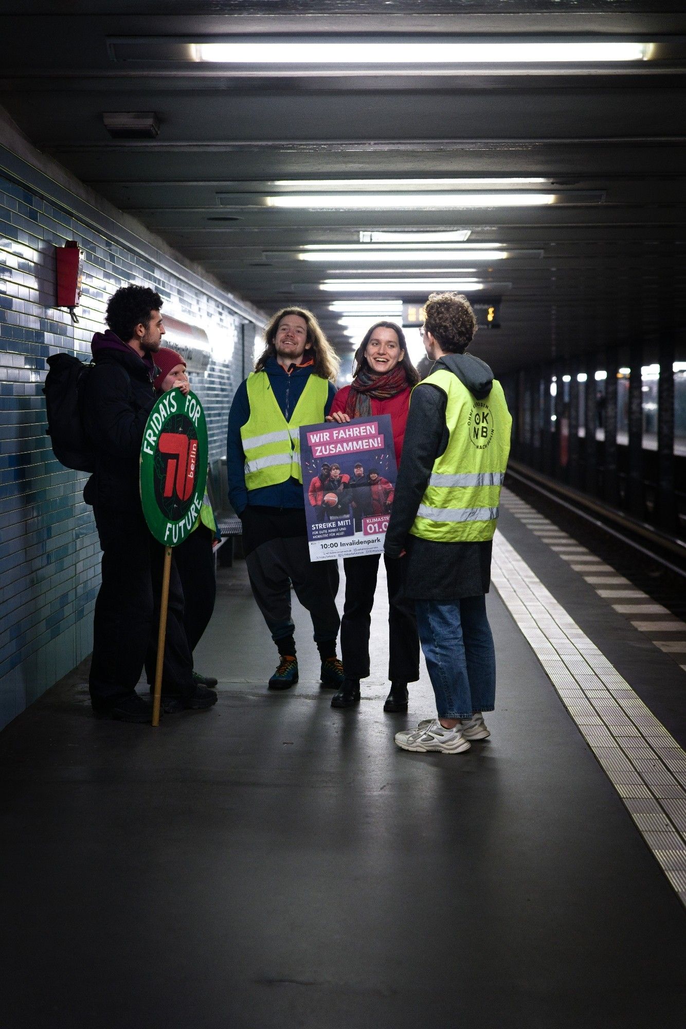 Studis mit Wir-fahren-zusammen-Plakat auf einem U-Bahnsteig