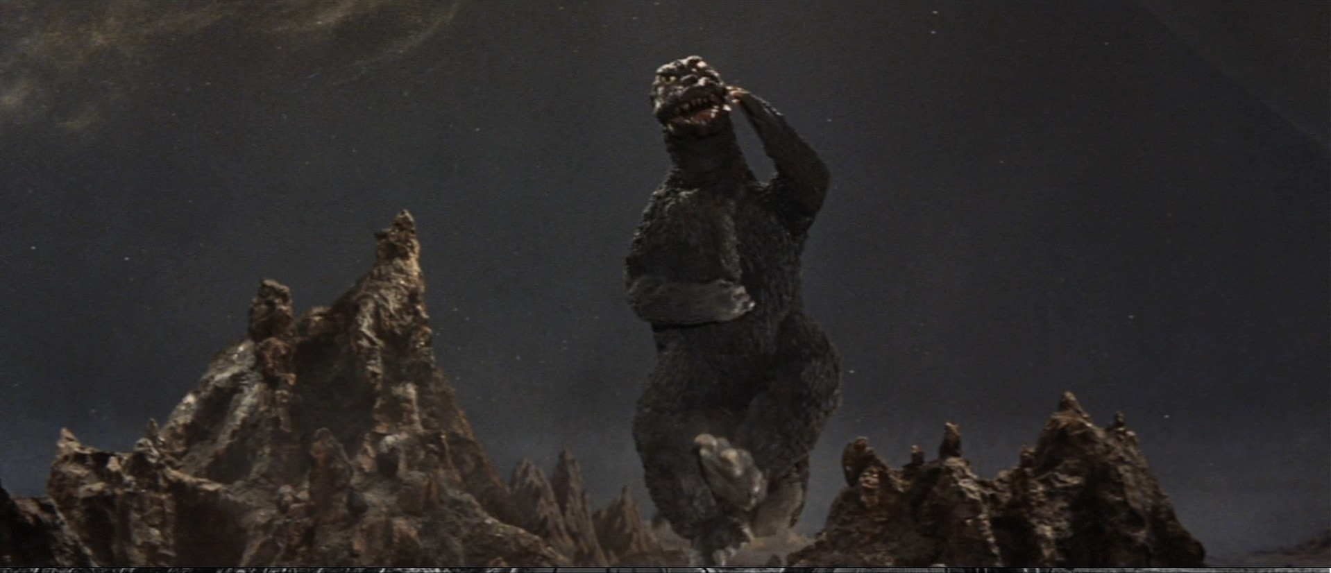 Godzilla celebrating a happy moment, having defeated King Ghidorah. It is leaping into the air and posing in a triumphant, yet silly way, to the delight of all.