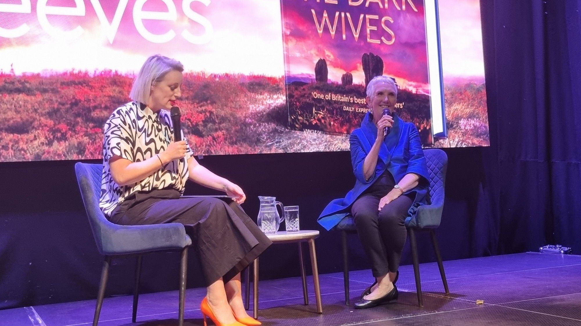 Steph McGovern interviewing Amn Cleeves. The backdrop is the cover of "The Dark Wives."