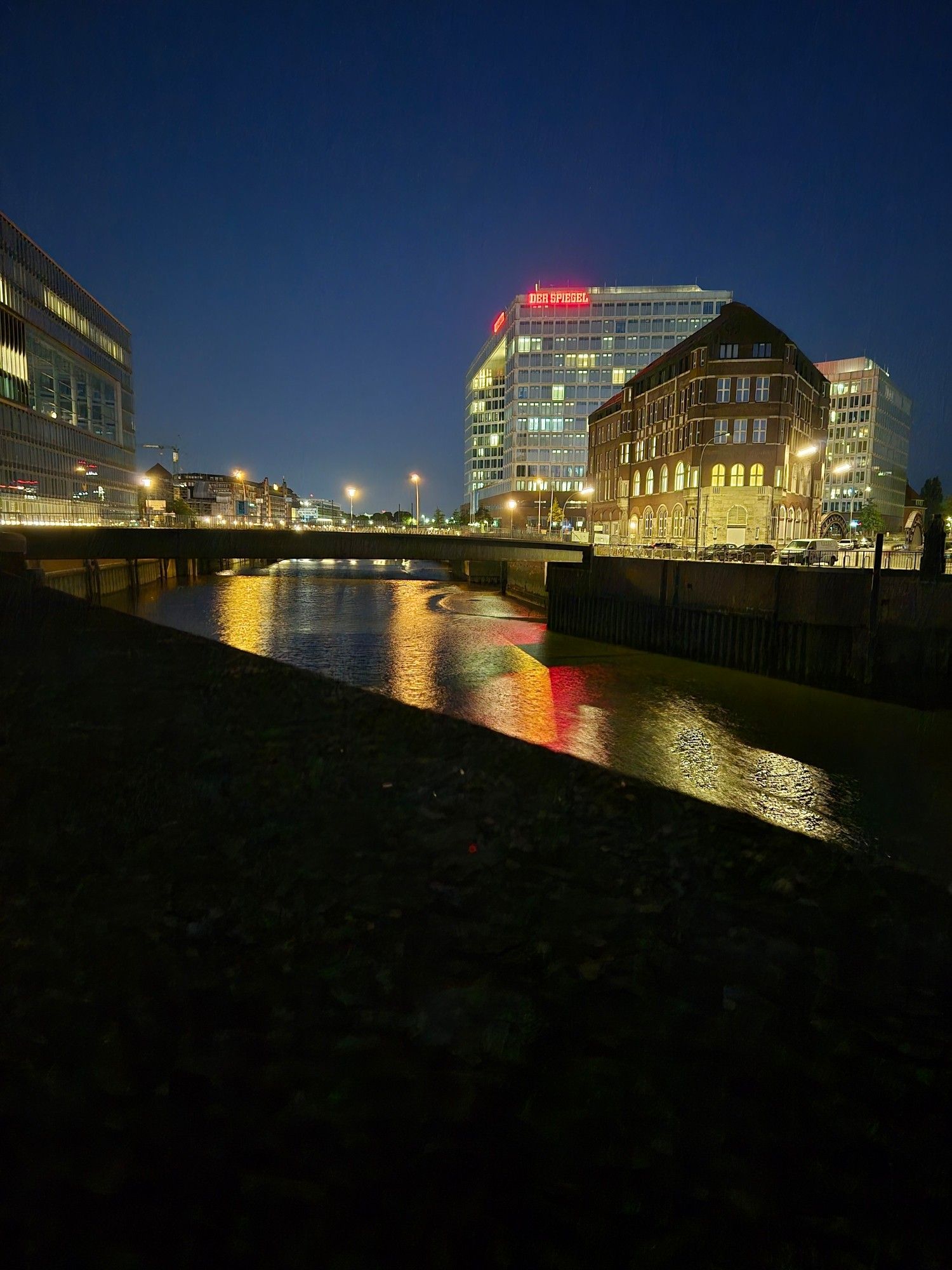 Blick auf das Spiegel Gebäude in Hamburg bei Nacht. Die beleuchteten Häuser spiegeln sich im Wasser und schimmern in der Dunkelheit