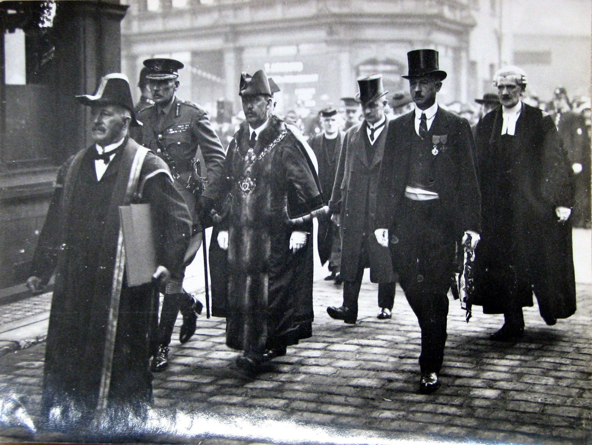 7th December 1924 at Keighley.
The smartly dressed war memorial party walks along the setts of Town Hall Street  towards Keighley War Memorial.
The party includes Lieutenant General Harington, Keighley Mayor R. Calverley and Monsieur G. Ducornet, Maire of Poix du Nord. Behind them walks Mr Newman King, Chairman of the War Memoirlal Committee and the Town Clerk Smith Terry.
Leading them all is the roll of honour book, carried by the Borough Treasurer.
They are all wearing uniform, or their robes of office.

Photo source: Keighley Library.