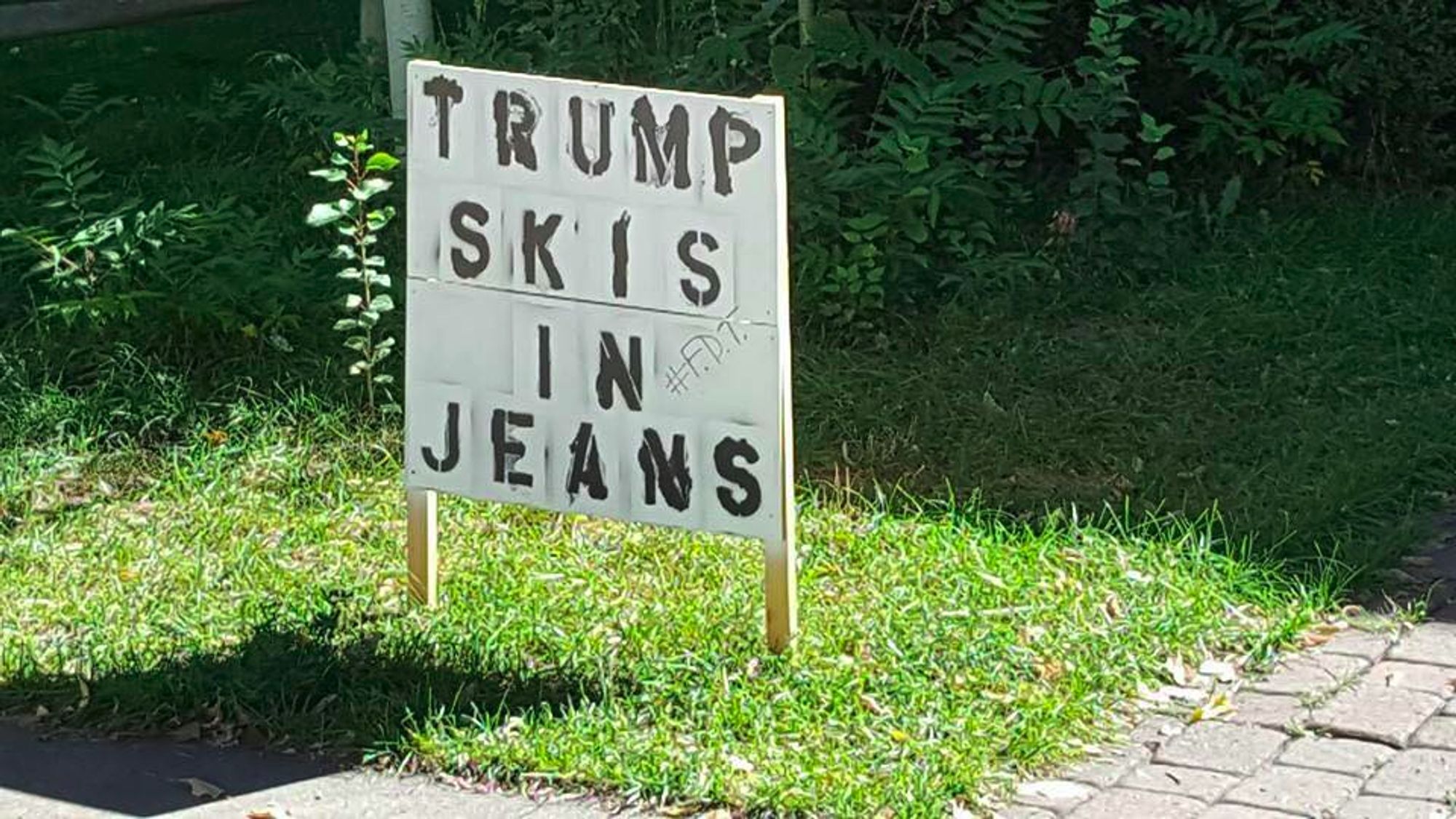 Handmade yard sign reads TRUMP SKIS IN JEANS with add-on graffiti #F.D.T. which I presume means Fuck Donald Trump.